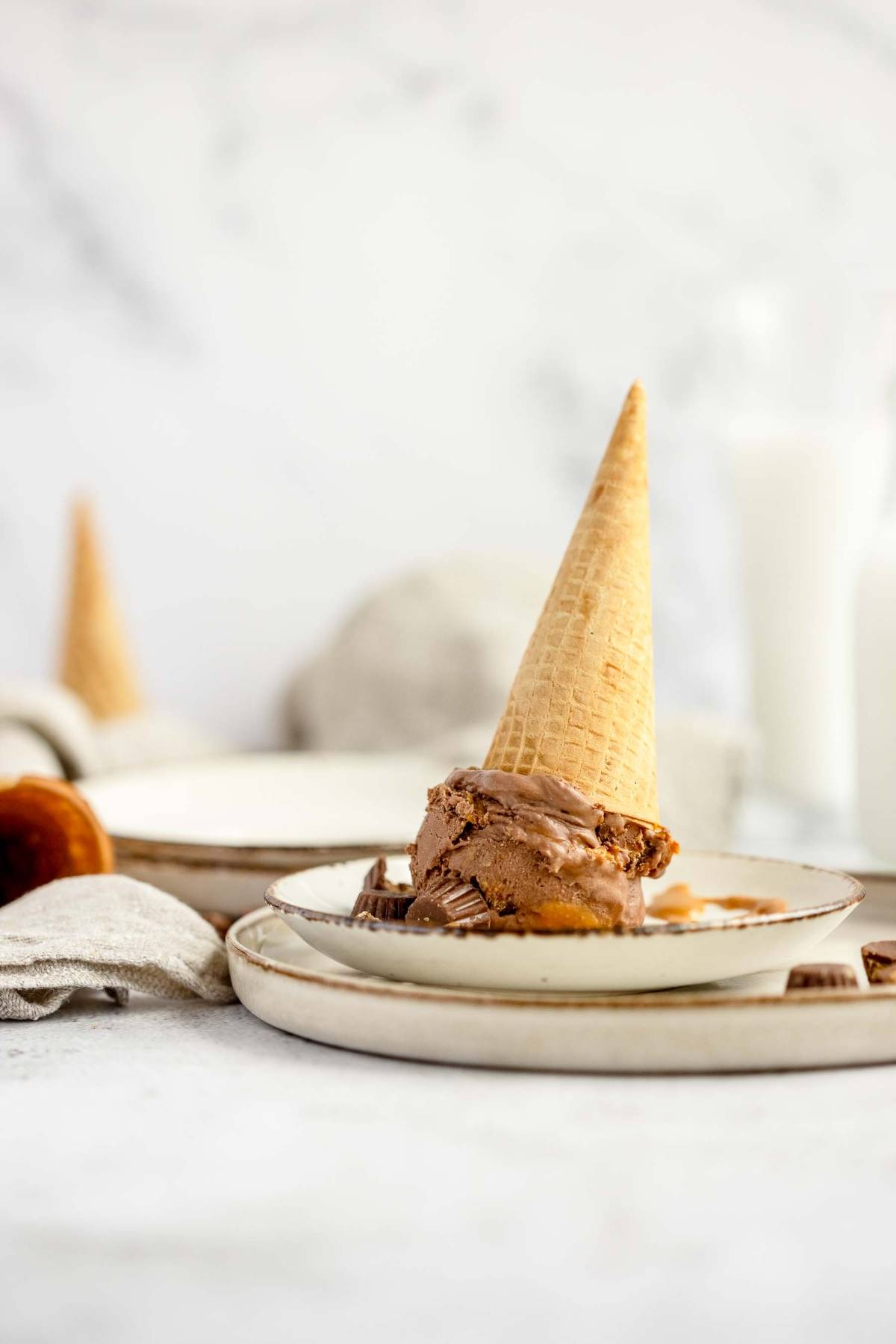 No Churn Chocolate Peanut Butter Cup Ice Cream with an upside-down cone on a plate, and another cone in the background.