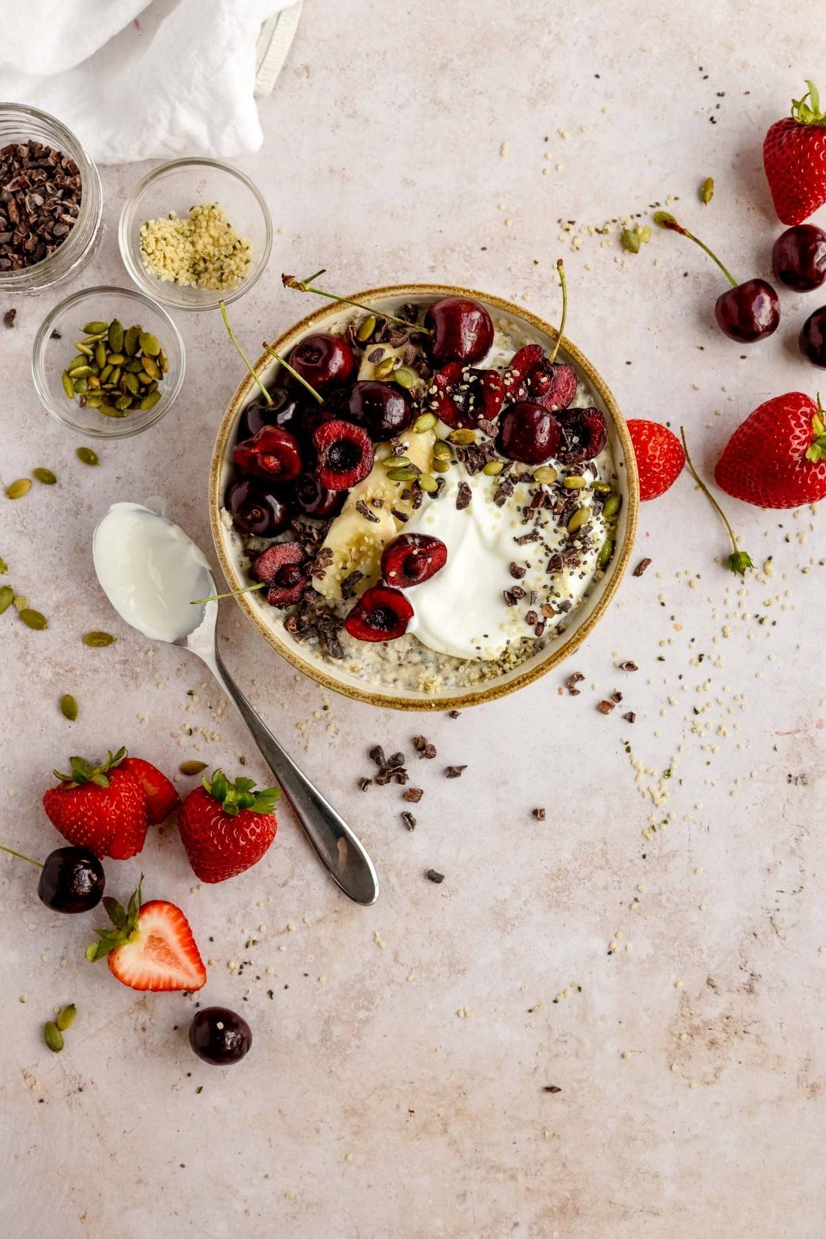 Bowl of yogurt topped with cherries, seeds, cacao nibs, and surrounded by strawberries—perfect inspiration for healthy oatmeal breakfast or creative oatmeal bowl toppings.