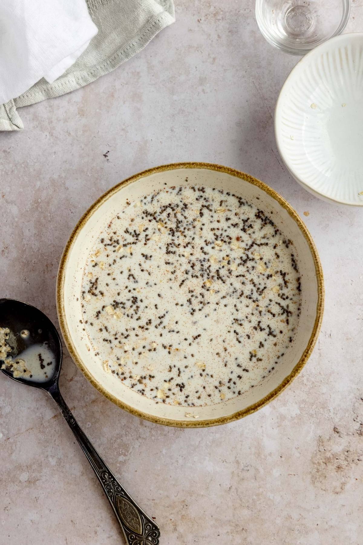 A bowl of creamy soup with black pepper, a spoon, and an empty dish on a light countertop—perfect inspiration for exploring healthy oatmeal breakfast ideas and creative oatmeal bowl toppings.