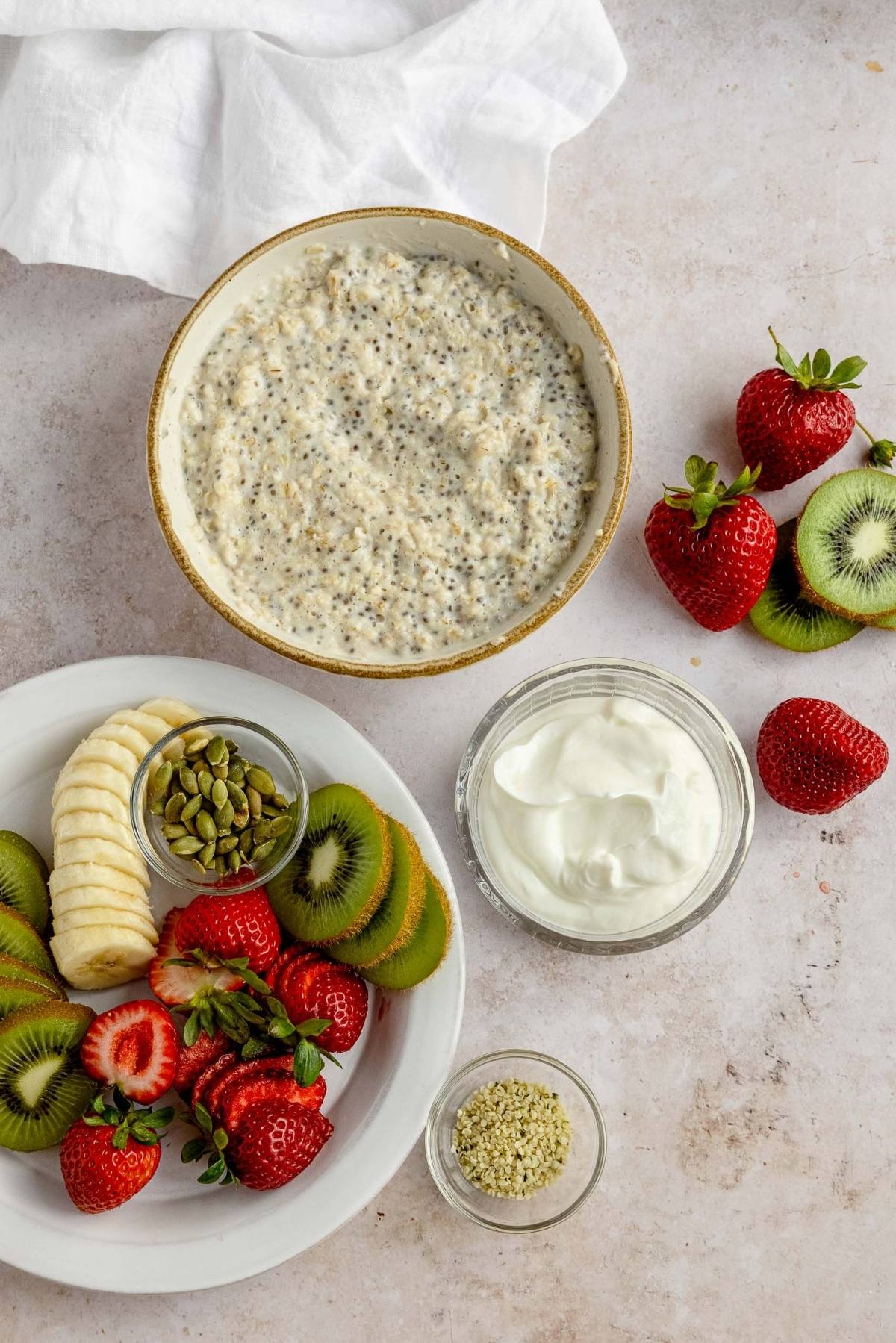 A bowl of chia pudding with yogurt, strawberries, kiwi, banana, pumpkin seeds, and hemp seeds on the side—just like you’d find in guides on oatmeal bowl toppings or oatmeal with fruit for breakfast.