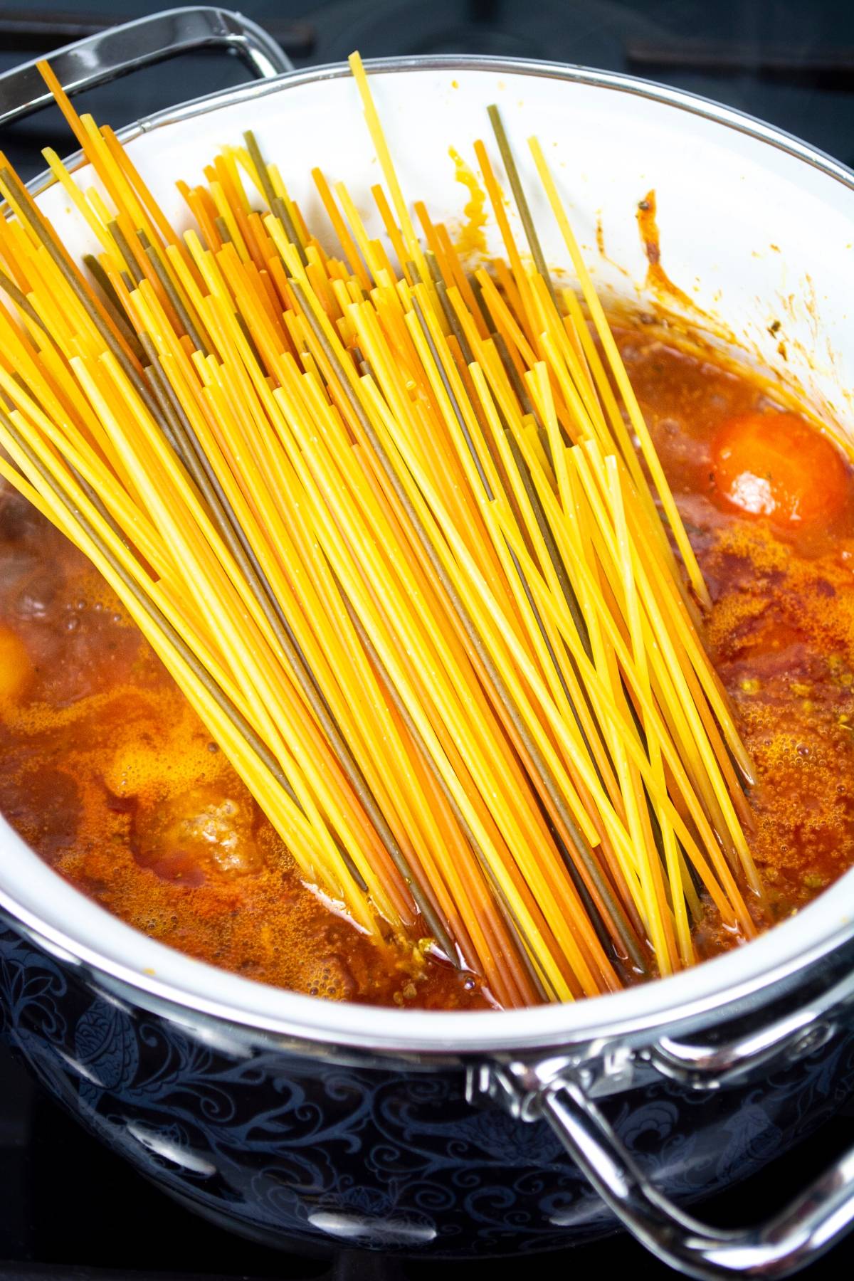 Uncooked spaghetti noodles in a pot of tomato sauce, starting to cook on a stovetop—perfect for an easy one pot Mediterranean pasta meal.