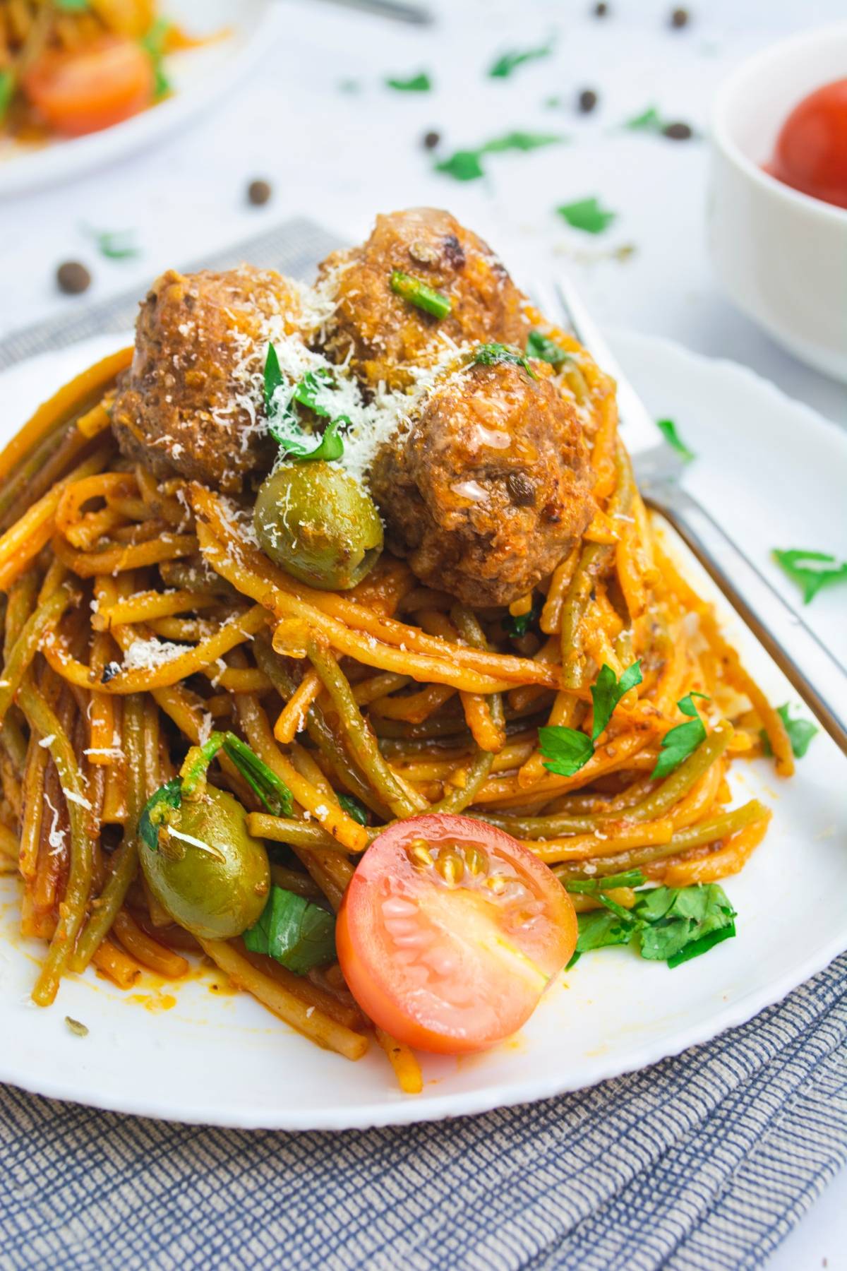 Spaghetti with meatballs, olives, tomato sauce, grated cheese, and fresh parsley on a white plate—an easy one pot Mediterranean pasta perfect for simple yet delicious meals.