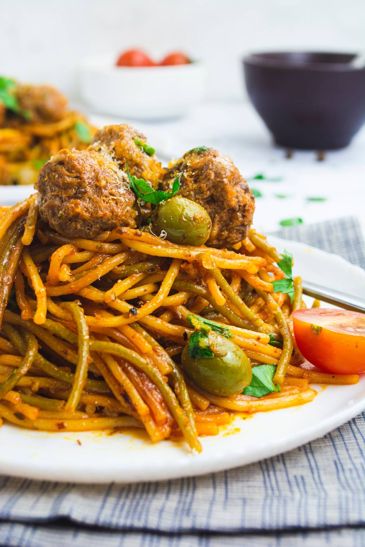 Spaghetti with meatballs, green olives, and tomato sauce, garnished with herbs on a white plate—a delicious Mediterranean spaghetti and meatballs dish.