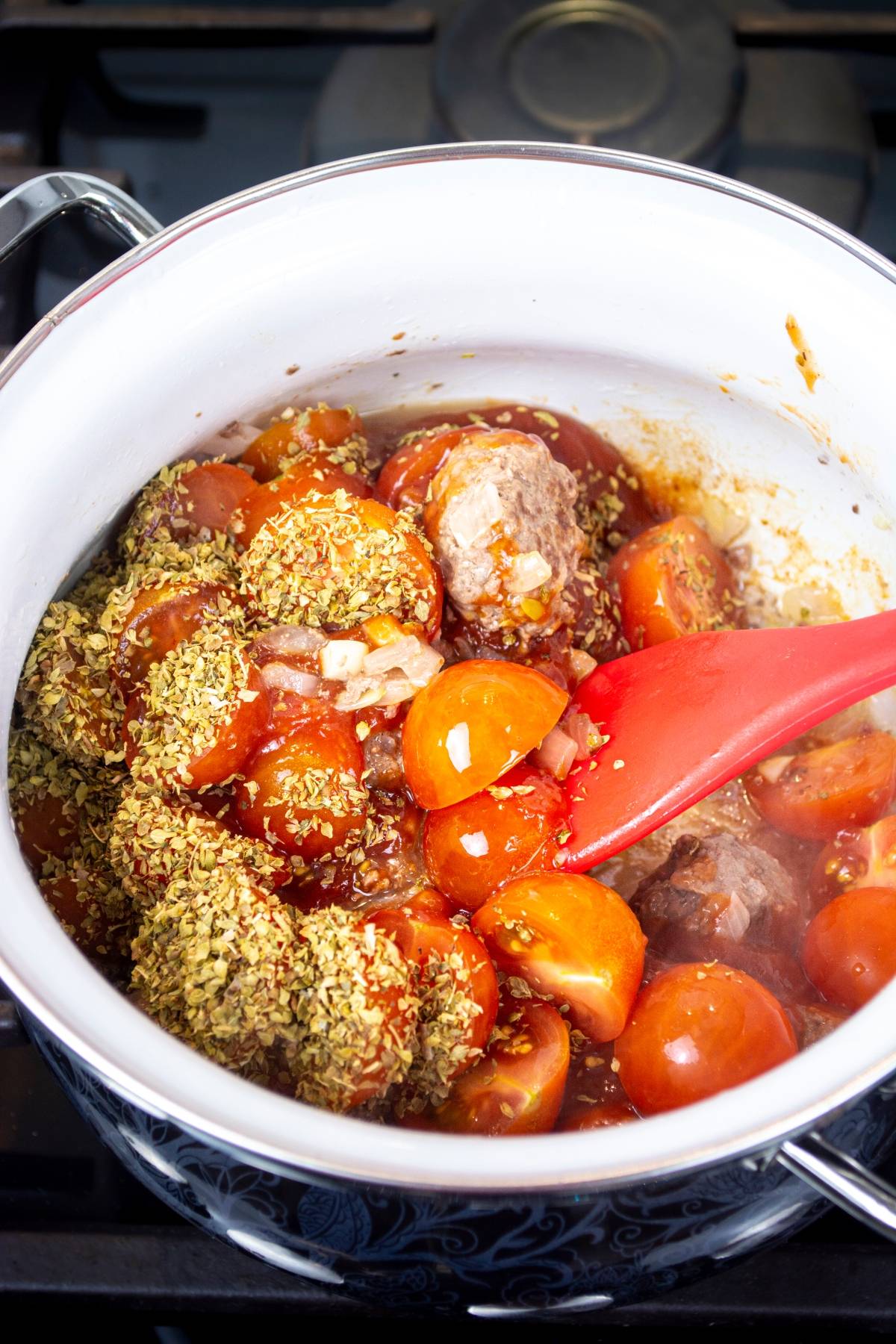 Chunks of tomato, beef, onions, and herbs cook in a white pot, stirred with a red spatula—the perfect base for an Easy one pot pasta inspired by Mediterranean flavors.