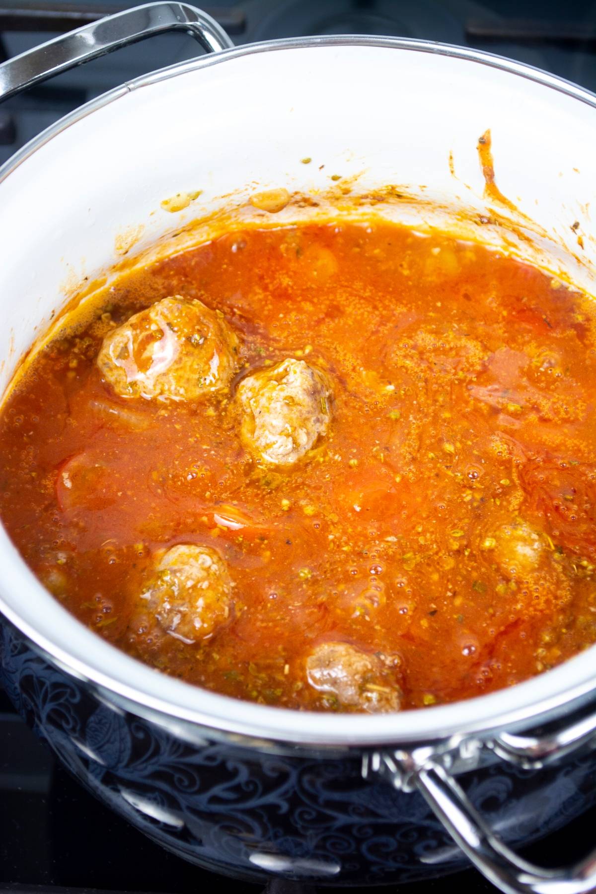 Meatballs simmering in red tomato sauce inside a white pot on a stovetop, perfect for an easy one pot pasta with meatballs.