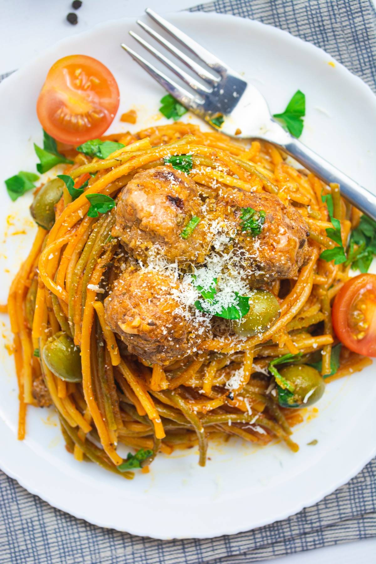 Spaghetti with meatballs, olives, tomatoes, parsley, and grated cheese on a white plate with a fork—an easy one pot pasta perfect for Mediterranean flavors in every bite.