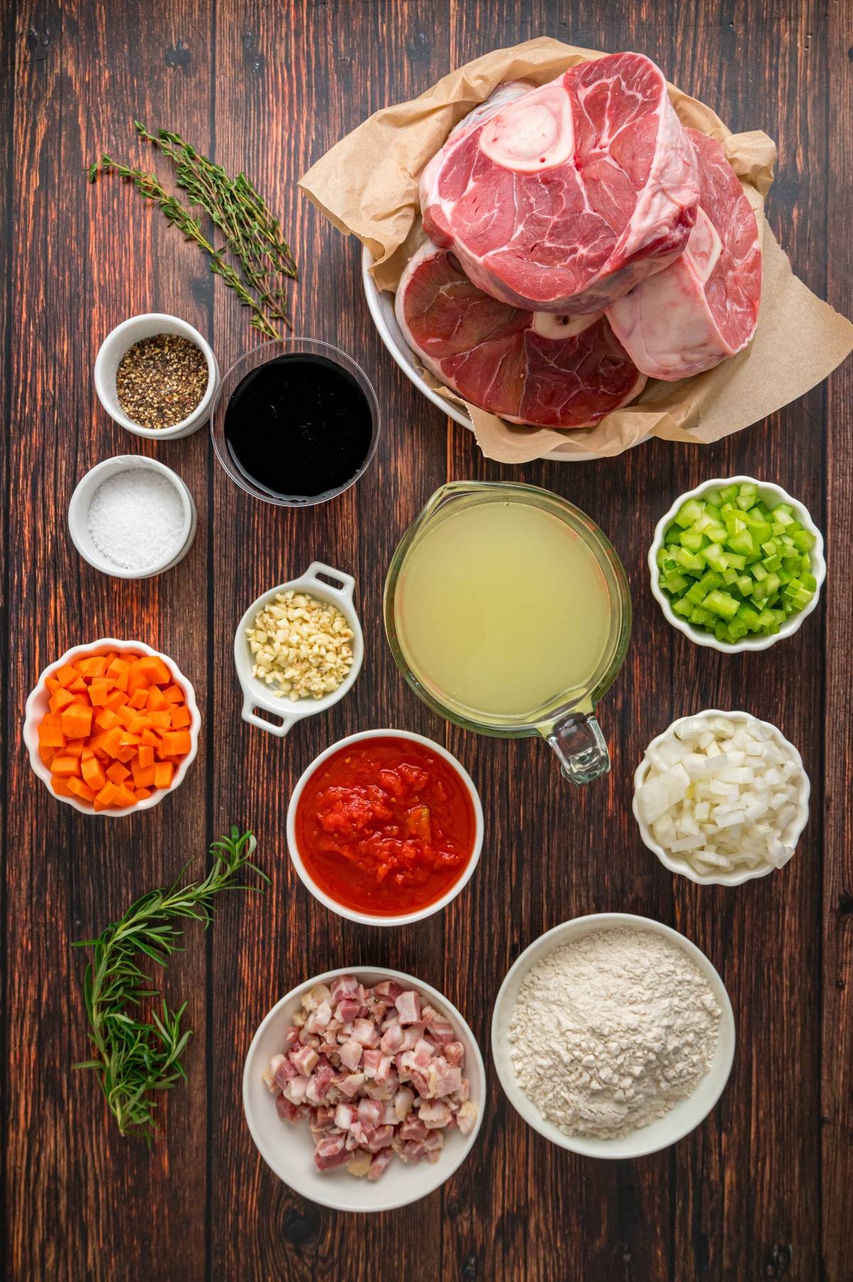 Ingredients for osso buco arranged on a wooden table, including meat, vegetables, broth, and seasonings.