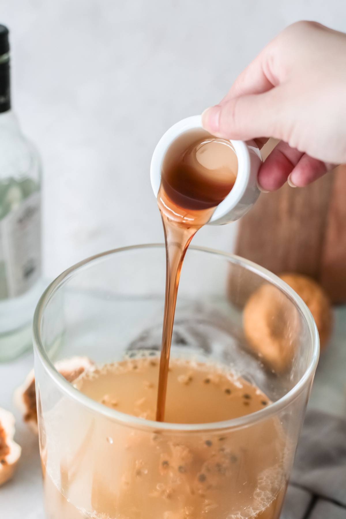 Hand pouring brown liquid from a small cup into a large glass bowl filled with creamy passion fruit margarita.