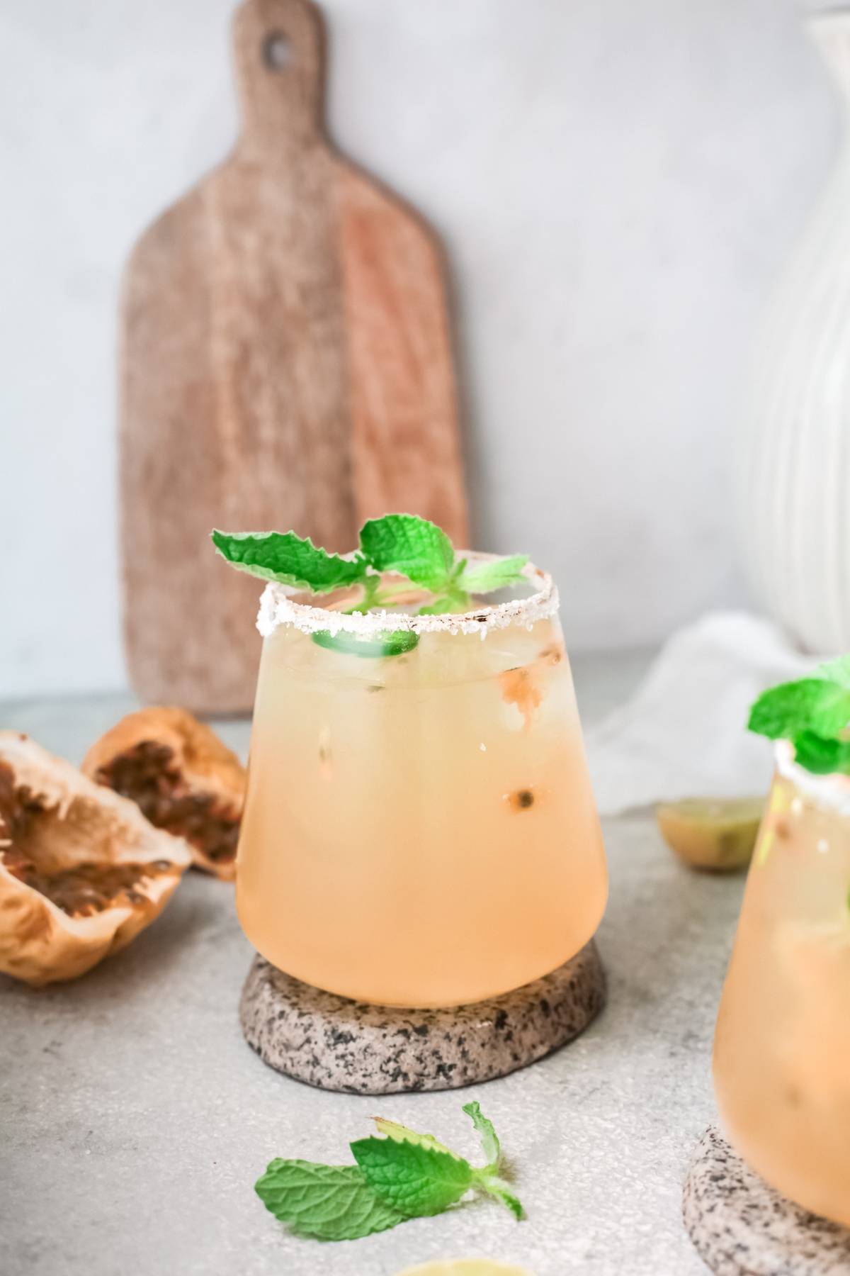 A light orange passion fruit cocktail in a glass with a salted rim, mint garnish, and ice sits on a stone coaster.