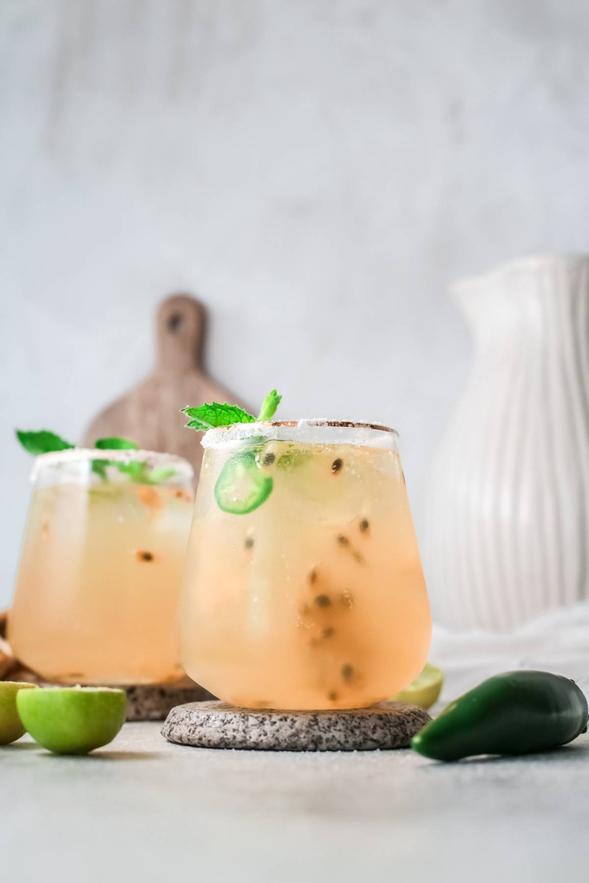 Two refreshing passion fruit cocktails with ice, mint, and jalapeño slices, garnished and set on stone coasters with limes nearby for a zesty twist.