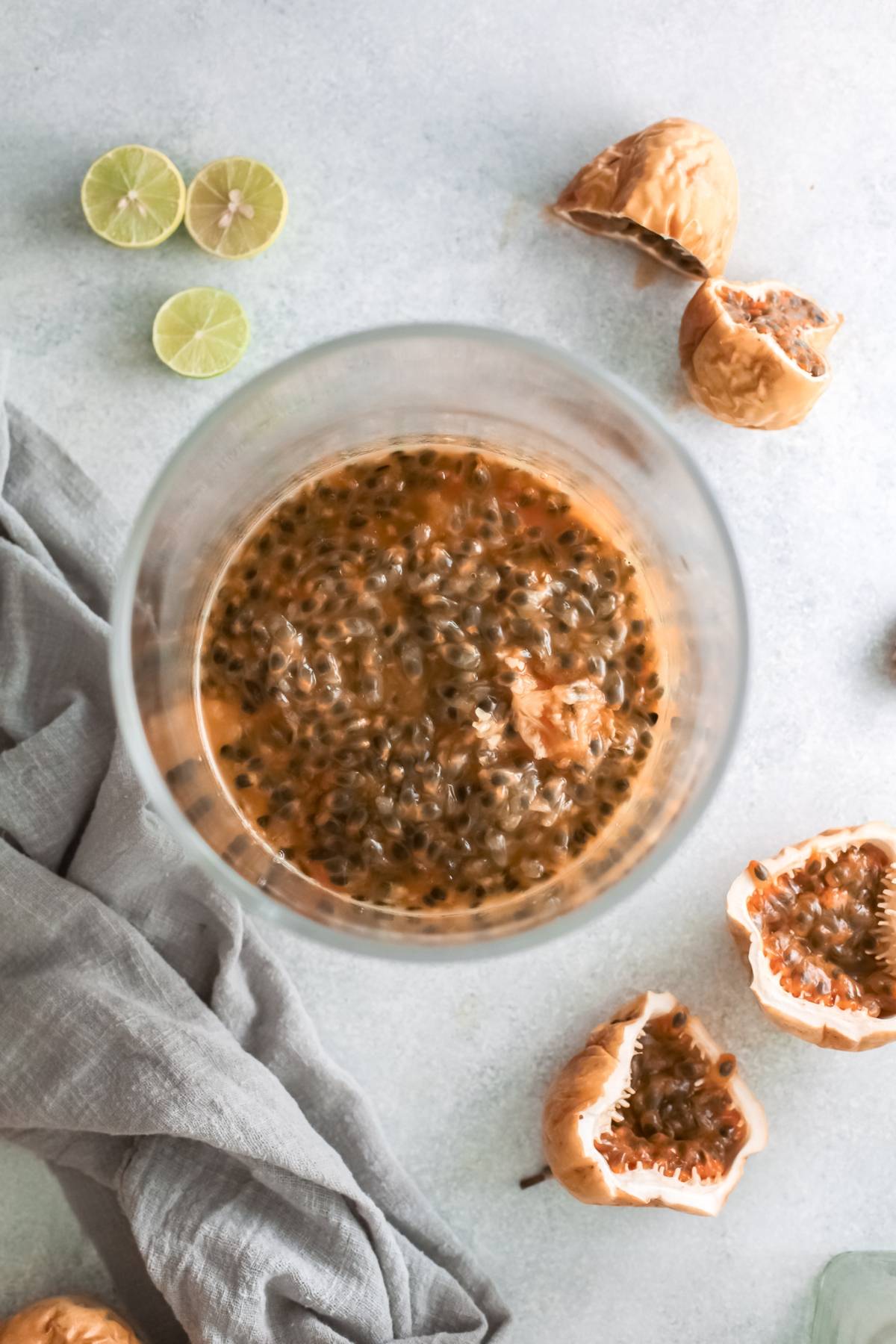 Top view of a glass filled with passion fruit pulp, surrounded by halved limes and passion fruit shells—a refreshing setup for a vibrant passion fruit margarita.
