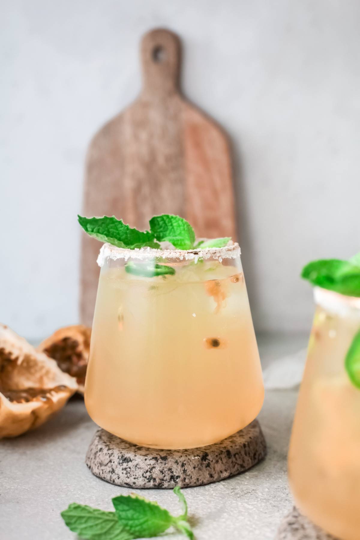 A light orange passion fruit cocktail in a glass with a salt rim and mint garnish, set on a stone coaster.