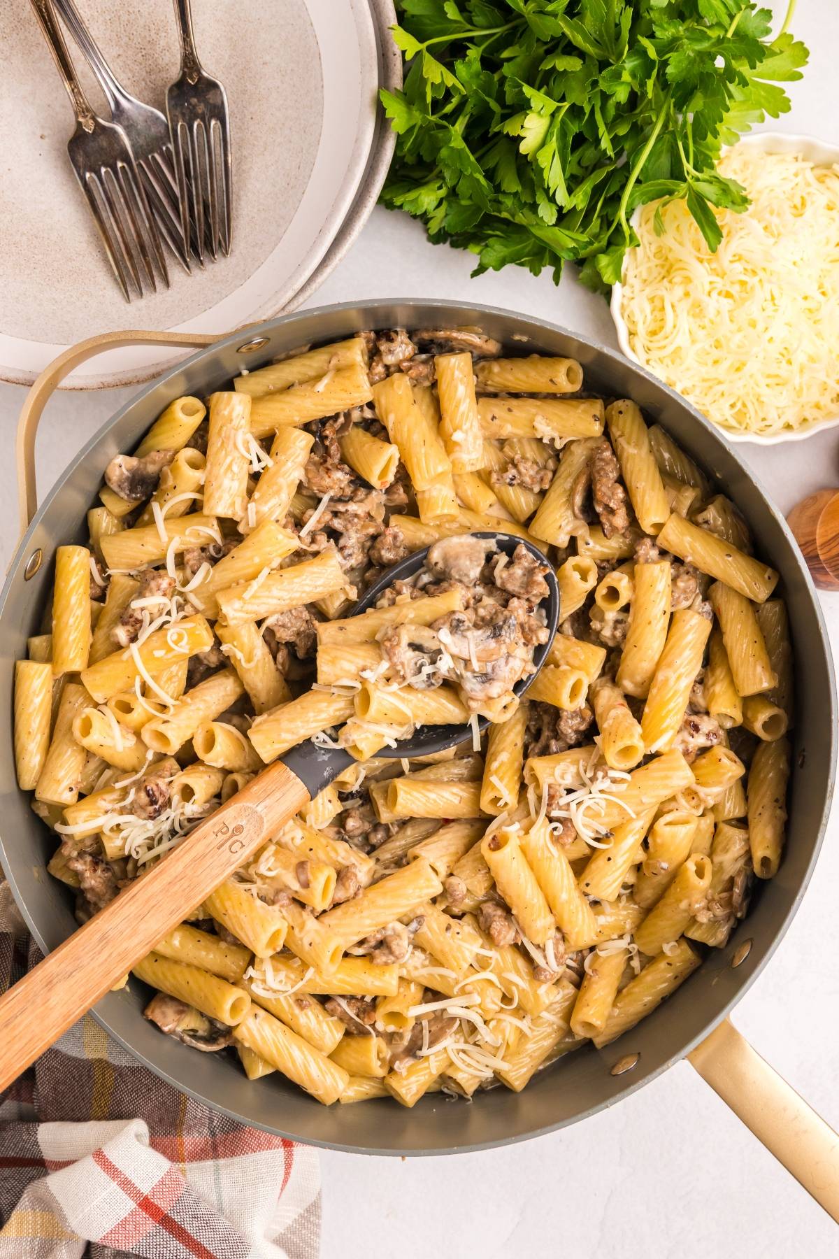 Large skillet filled with creamy rigatoni pasta, ground meat, mushrooms, and cheese, with a serving spoon.