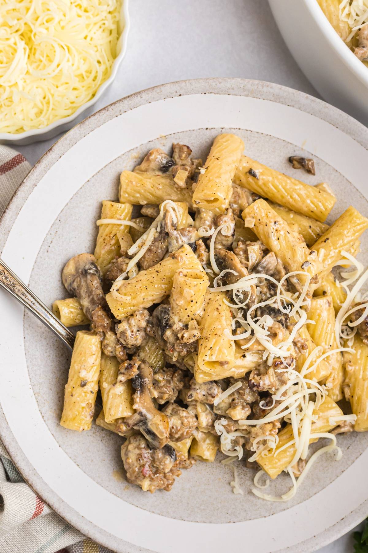 A plate of creamy rigatoni pasta with sausage, mushrooms, and shredded cheese on top.