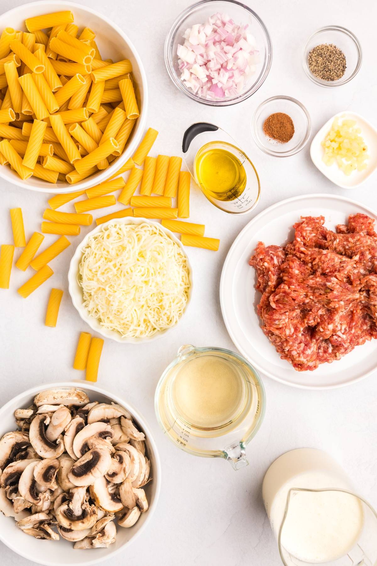 Uncooked rigatoni, ground meat, shredded cheese, sliced mushrooms, onions, garlic, cream, oil, and seasonings.