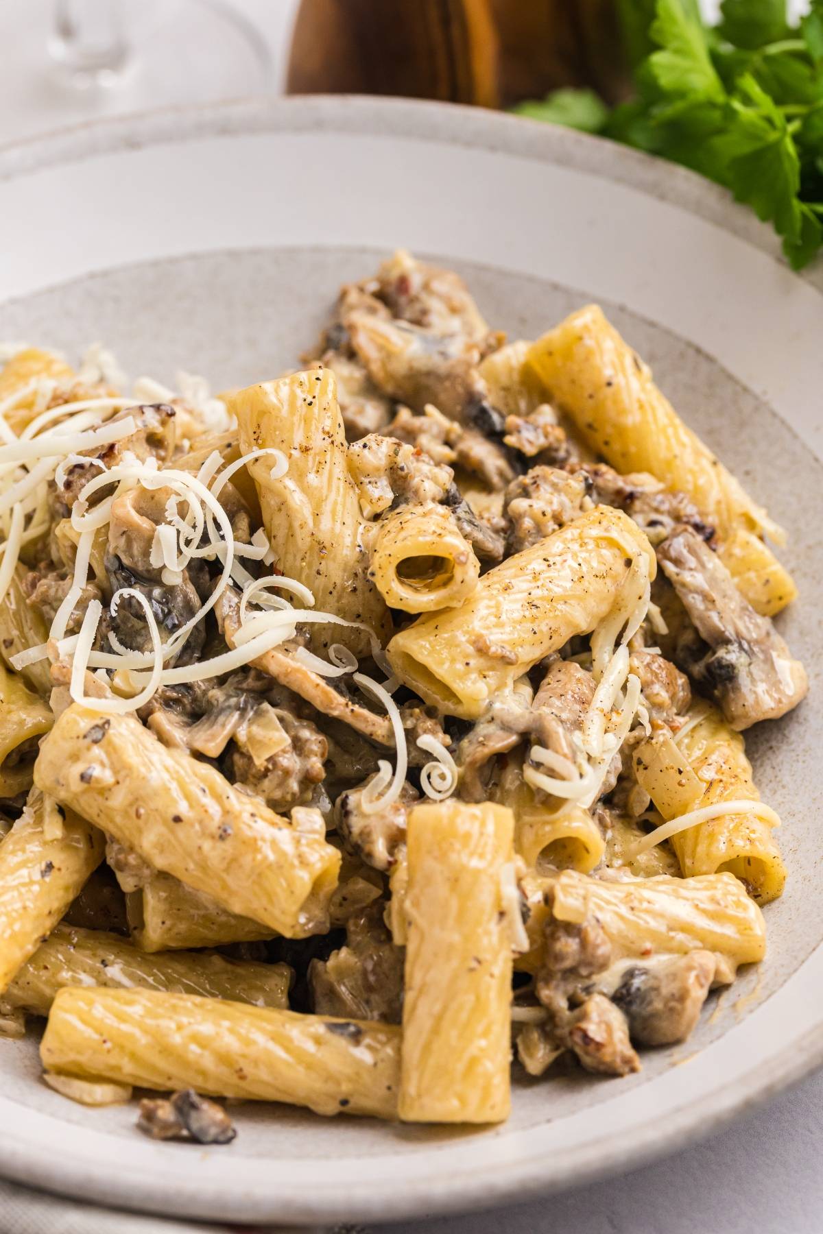 Rigatoni pasta with creamy mushroom sauce and grated cheese, served in a shallow bowl.