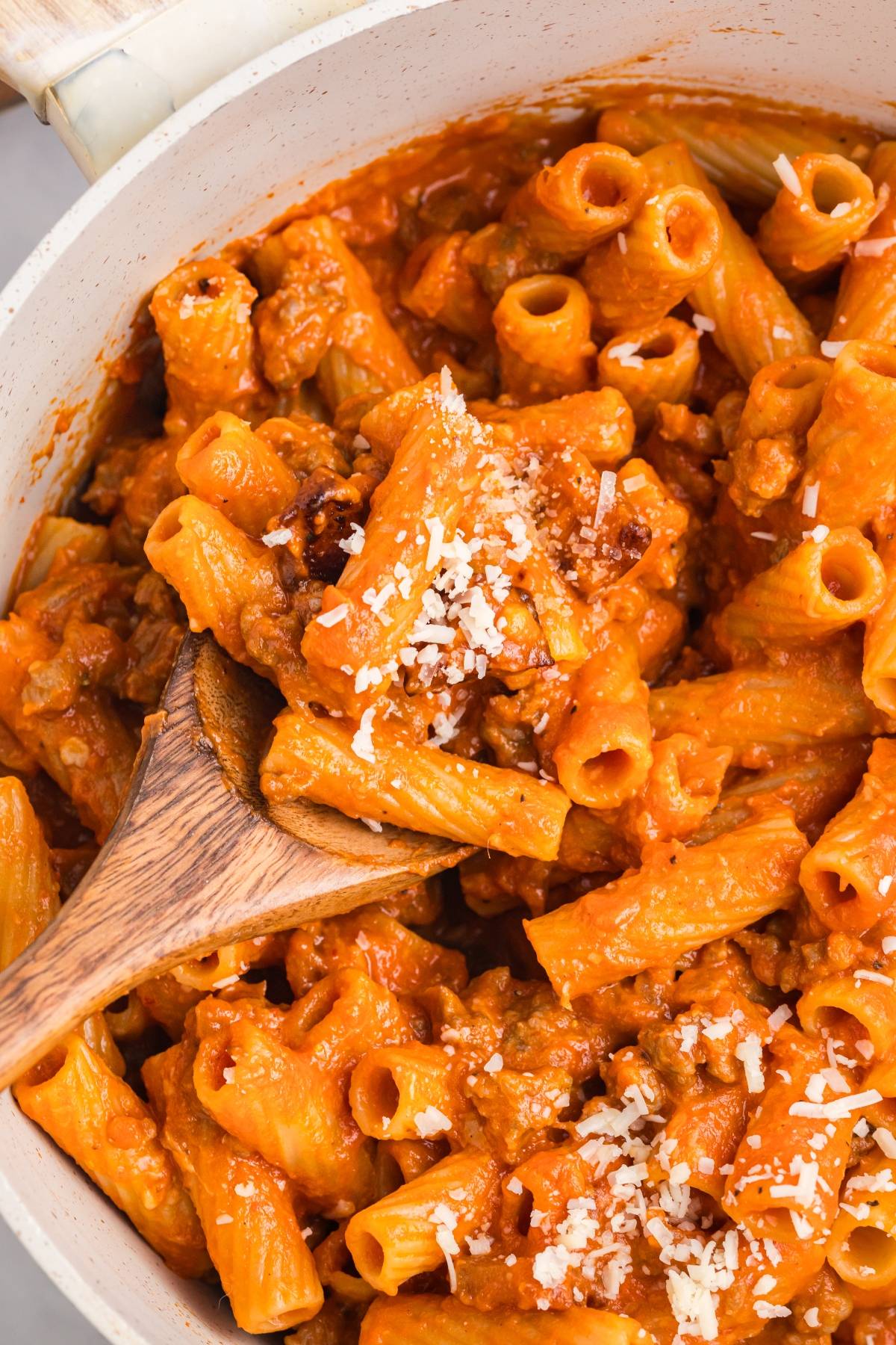 Rigatoni pasta in a rich tomato sauce with ground meat, topped with grated cheese, and served with a wooden spoon.