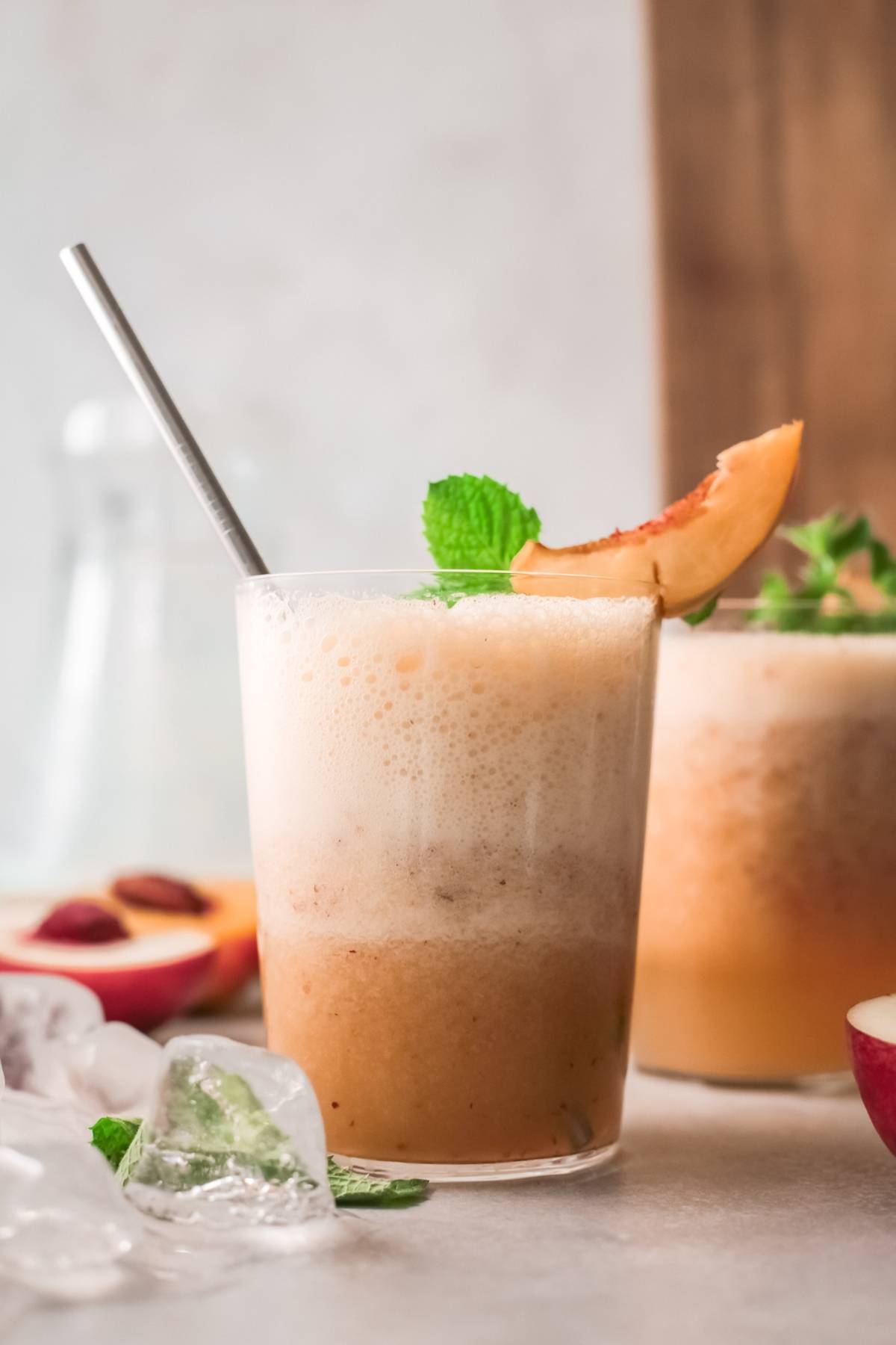 A frothy peach smoothie in a glass with a metal straw, garnished with mint and a peach slice—perfect as a refreshing non-alcoholic twist on the classic Bellini recipe.