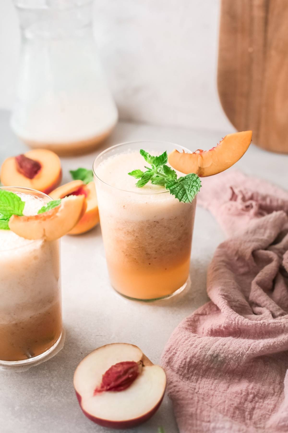 Two peach smoothies in glasses, garnished with peach slices and mint, surrounded by fresh peaches—perfect for a refreshing recipe with peach juice or as inspiration for your next Bellini recipe.
