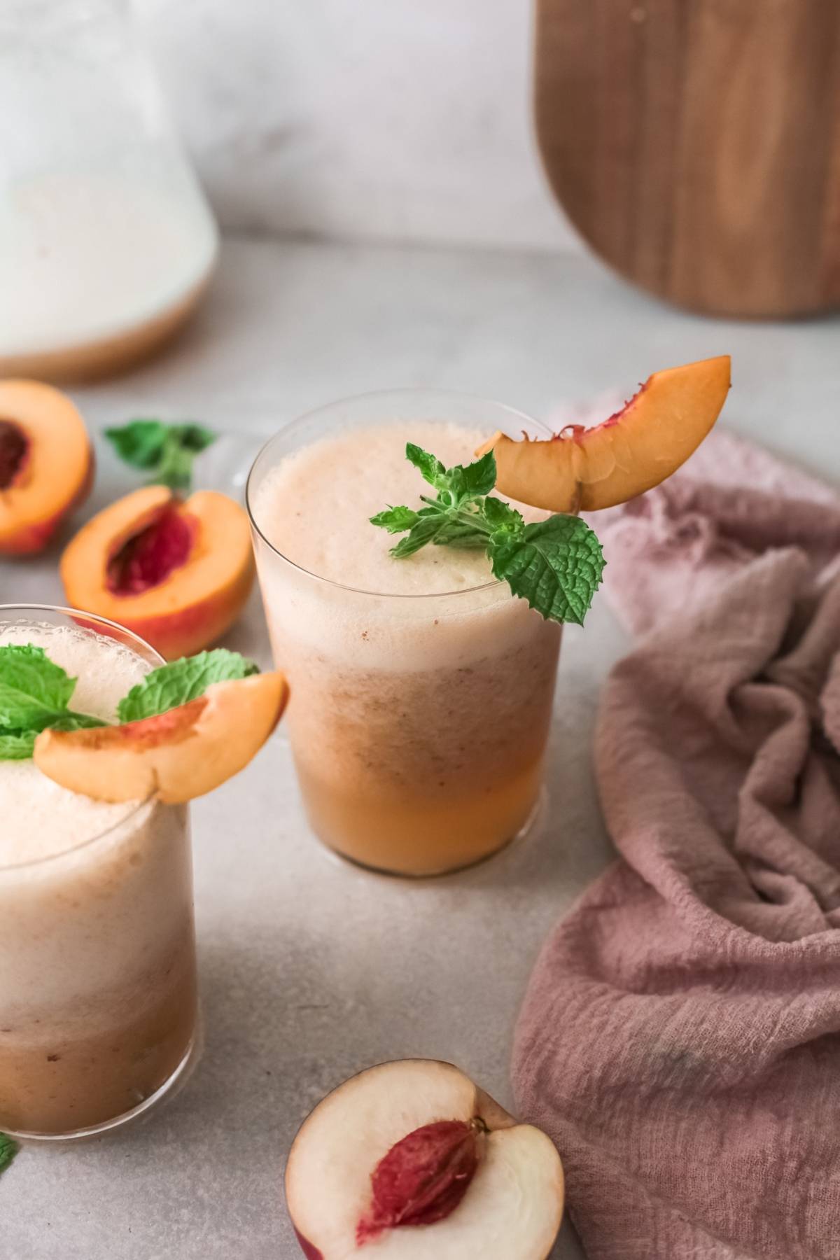 Two peach smoothies in glasses, garnished with peach slices and mint, surrounded by fresh peaches—perfect inspiration for your next peach bellini cocktail recipe.