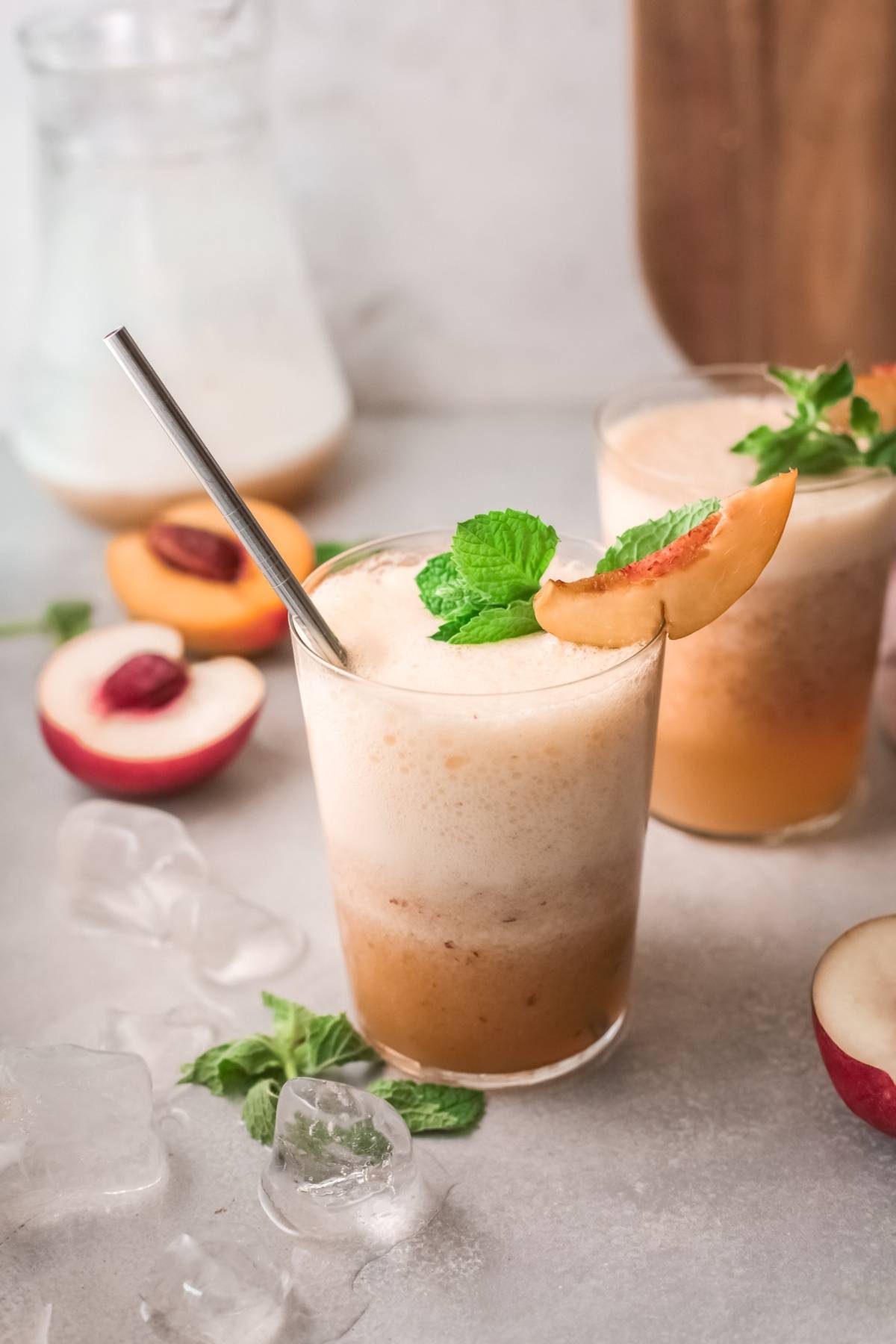 Iced peach smoothie with foam, inspired by a classic Bellini recipe, garnished with mint and a peach slice, served with a metal straw.