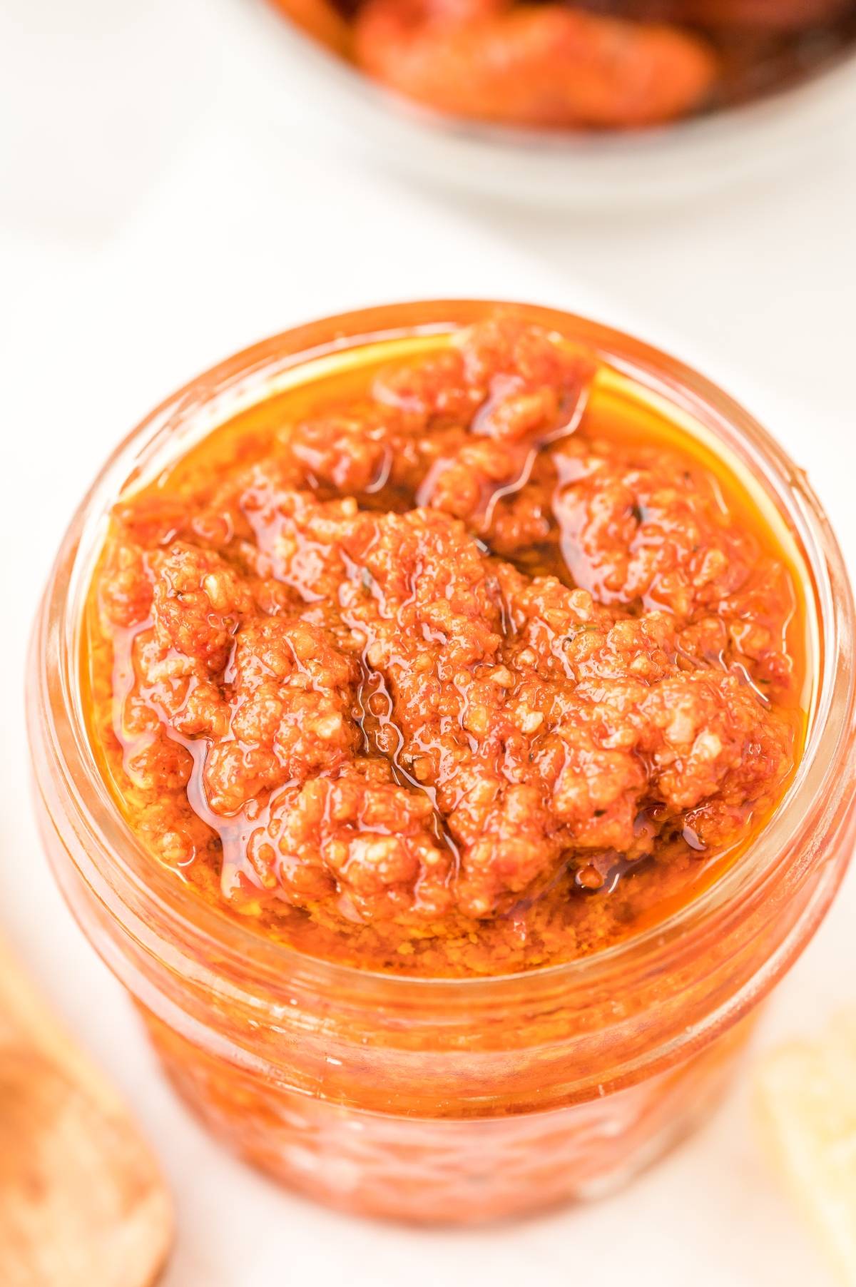A close-up of a glass jar filled with chunky red chili paste topped with oil, resembling a sun dried tomato pesto—perfect inspiration for your next red pesto recipe.