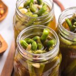Three jars filled with tangy pickled green beans and spices are viewed from above on a kitchen counter.