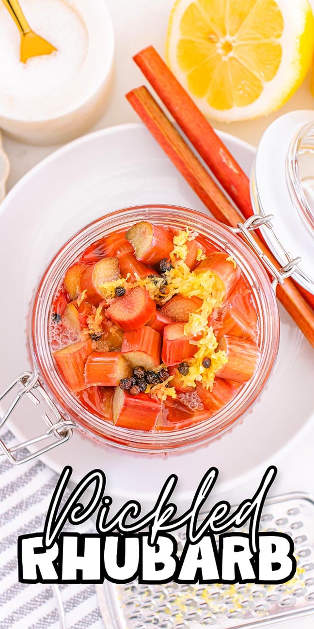 A jar of pickled rhubarb with peppercorns and lemon zest sits surrounded by fresh rhubarb stalks and lemon slices, showcasing the vibrant appeal of homemade pickled rhubarb.