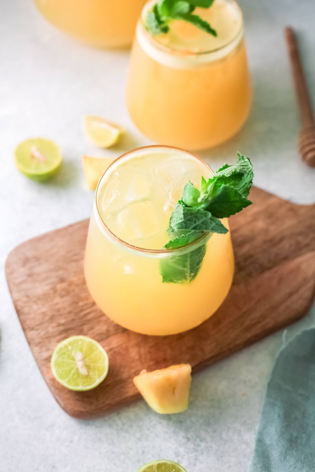 A glass of iced pineapple drink garnished with mint, with lime wedges and honey dipper nearby—a perfect summer drink with pineapple for a refreshing treat.