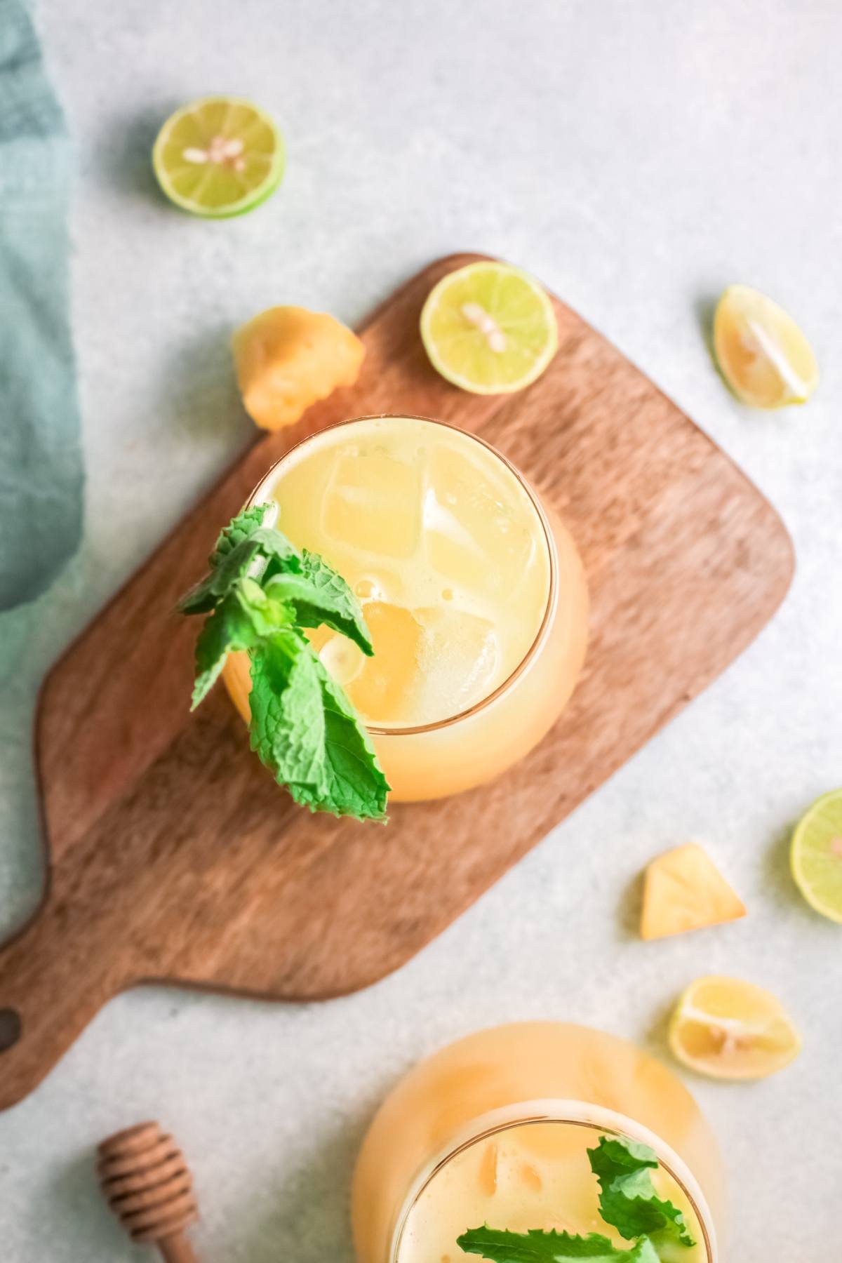 A glass of orange juice with ice and mint on a wooden board, surrounded by lime slices and pineapple pieces—perfect inspiration for a refreshing non-alcoholic drink recipe like Pineapple Agua Fresca.