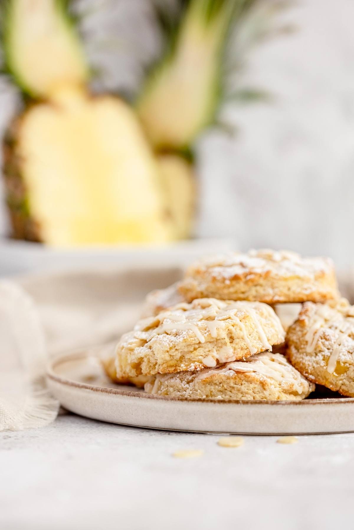A plate of glazed cookies is in focus, with a sliced pineapple blurred in the background—perfect inspiration for a recipe using crushed pineapple or creative tips for making scones.