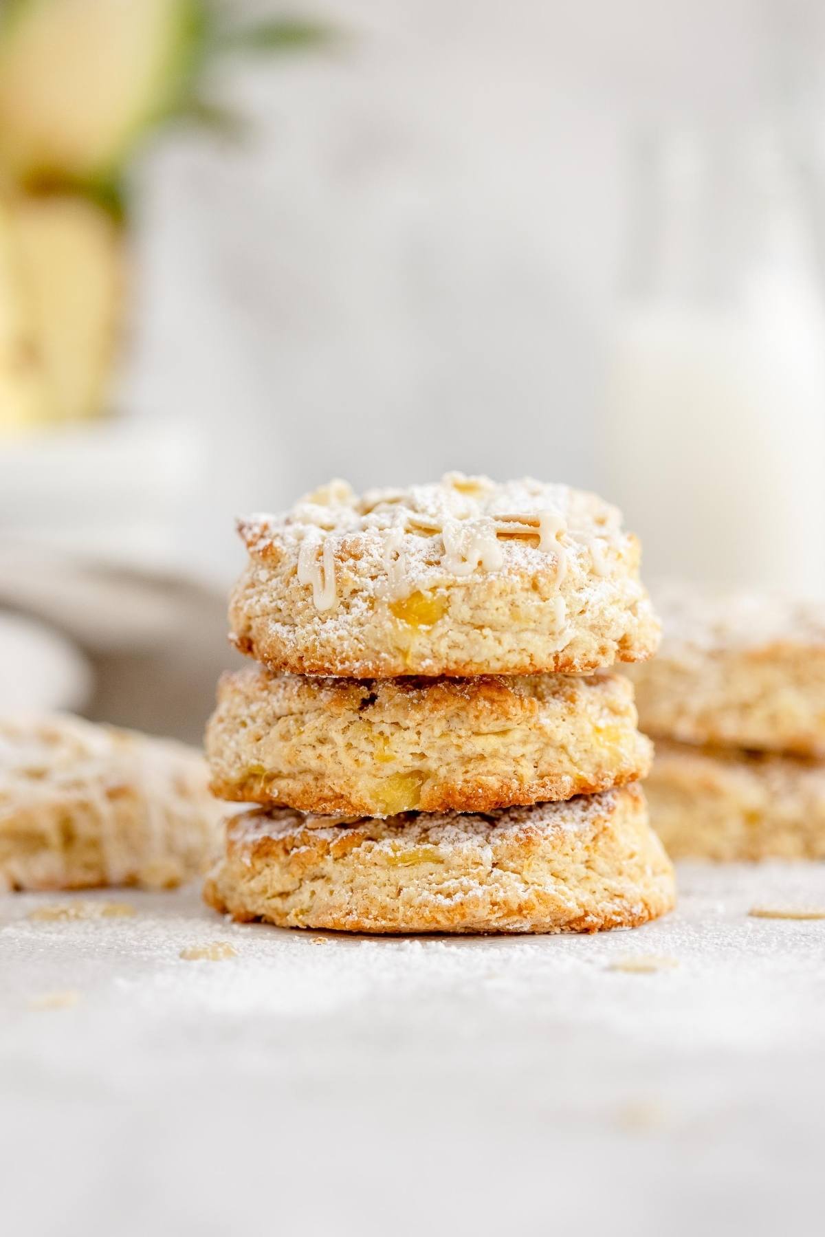 Three flaky scones made with pineapple are stacked on top of each other, dusted with powdered sugar on a light background.