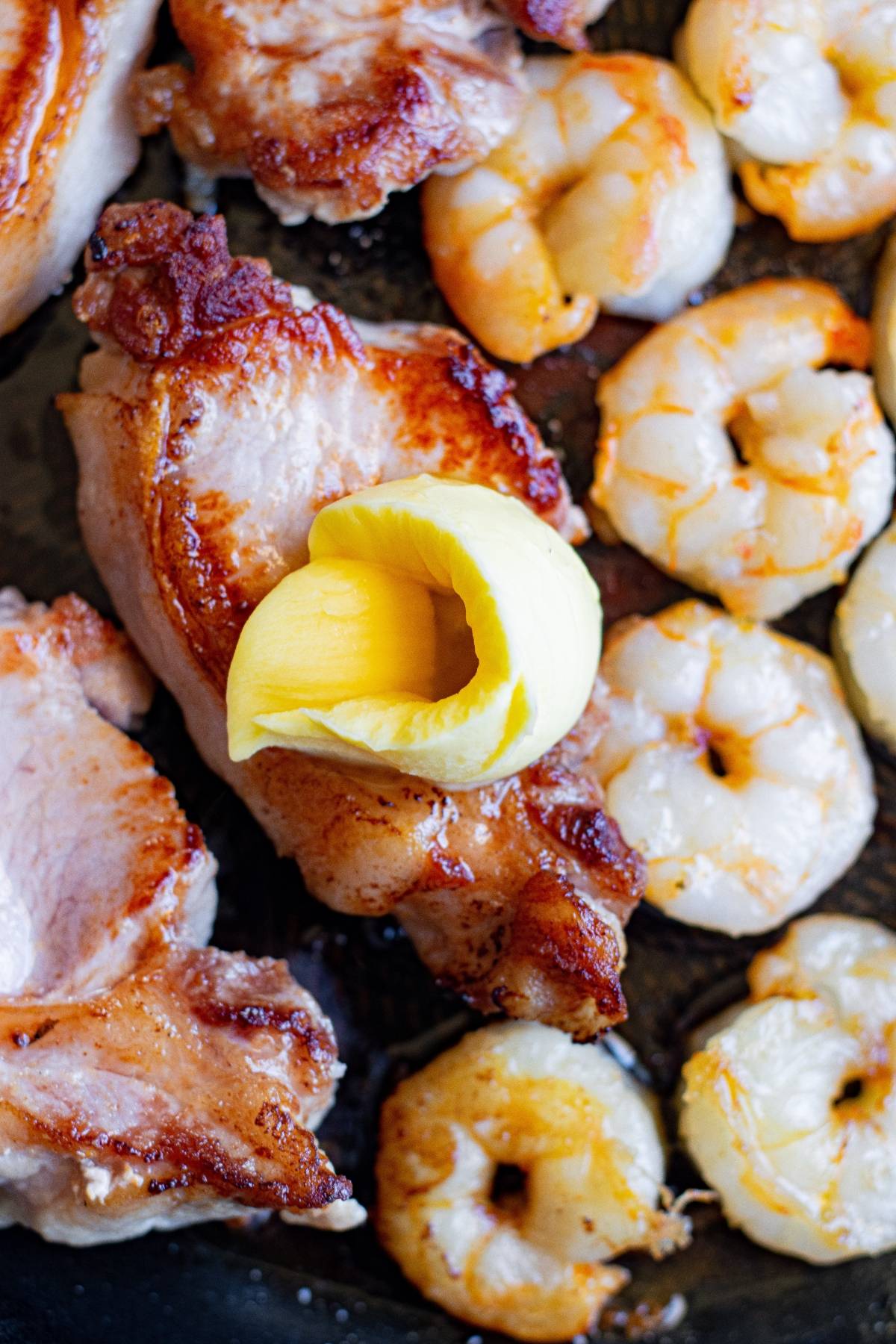 Grilled chicken and butter herbed shrimp in a pan with a curl of butter melting on top of a chicken piece.