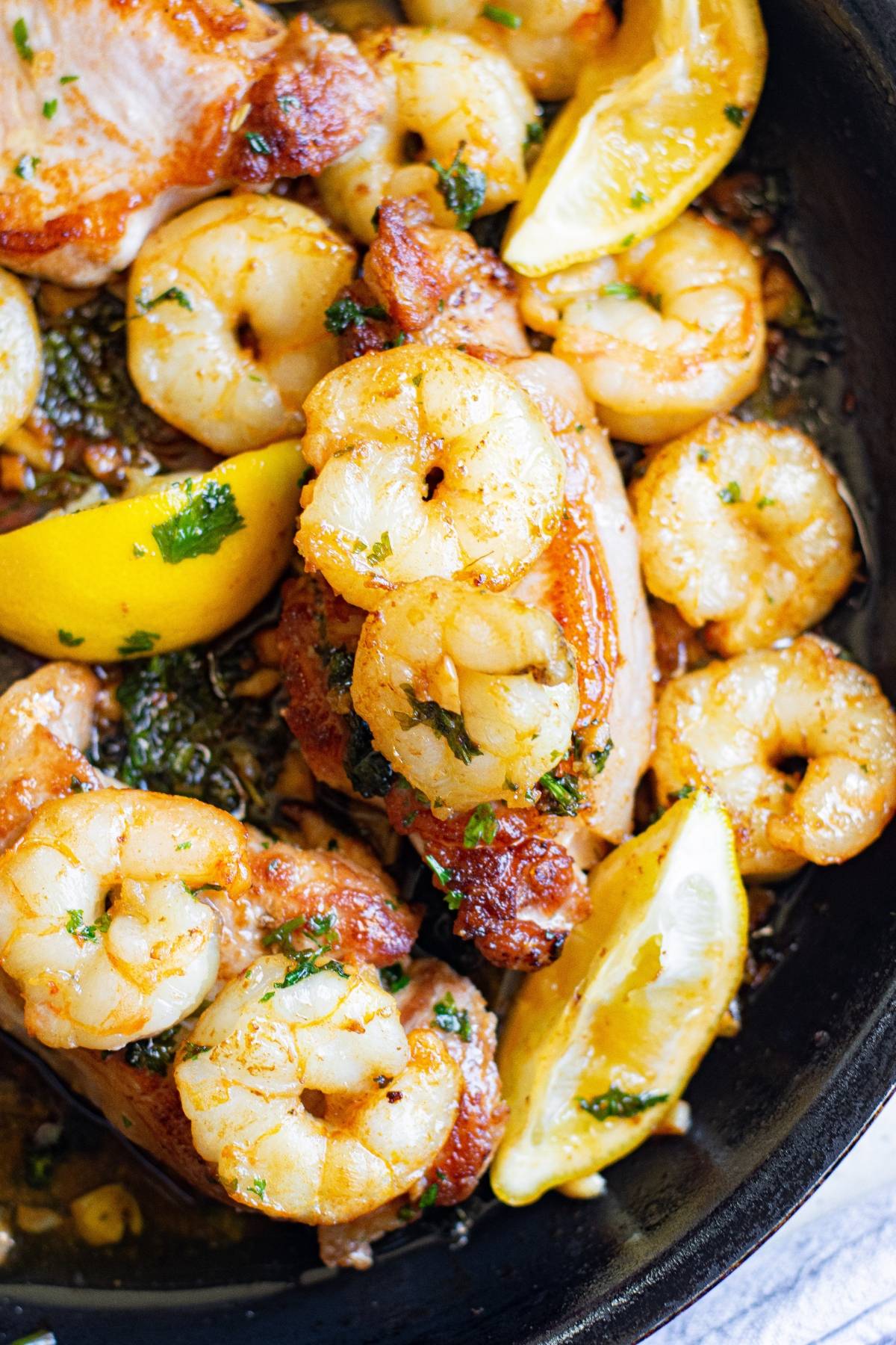 Enjoy a surf and turf twist with cooked shrimp and chicken, seasoned with fresh herbs and lemon wedges in a skillet.