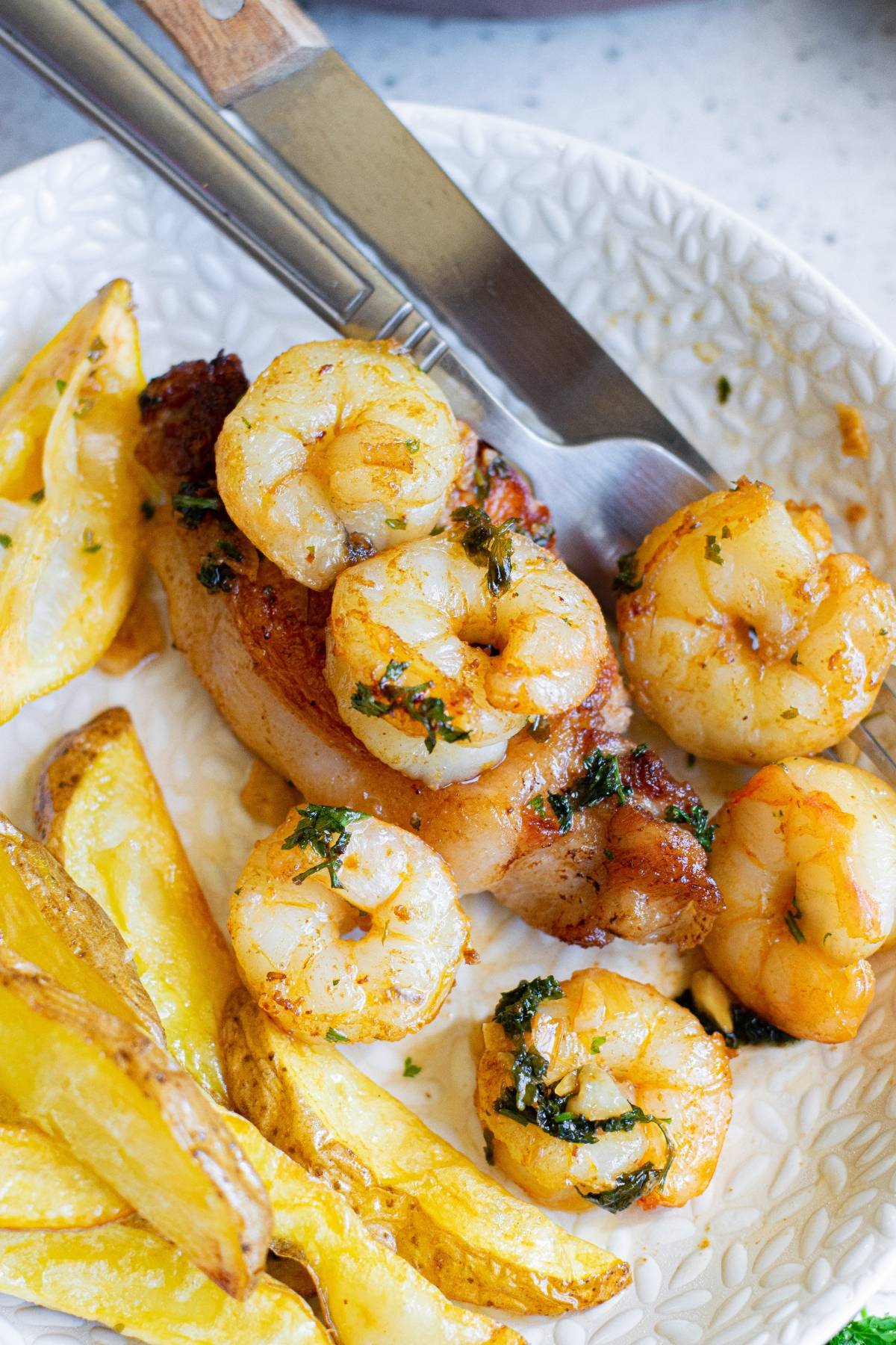 Grilled shrimp and chicken served with potato wedges on a white plate, capturing the essence of a classic surf and turf meal—perfect for those who enjoy a twist on traditional recipes. Knife and fork included for easy dining.