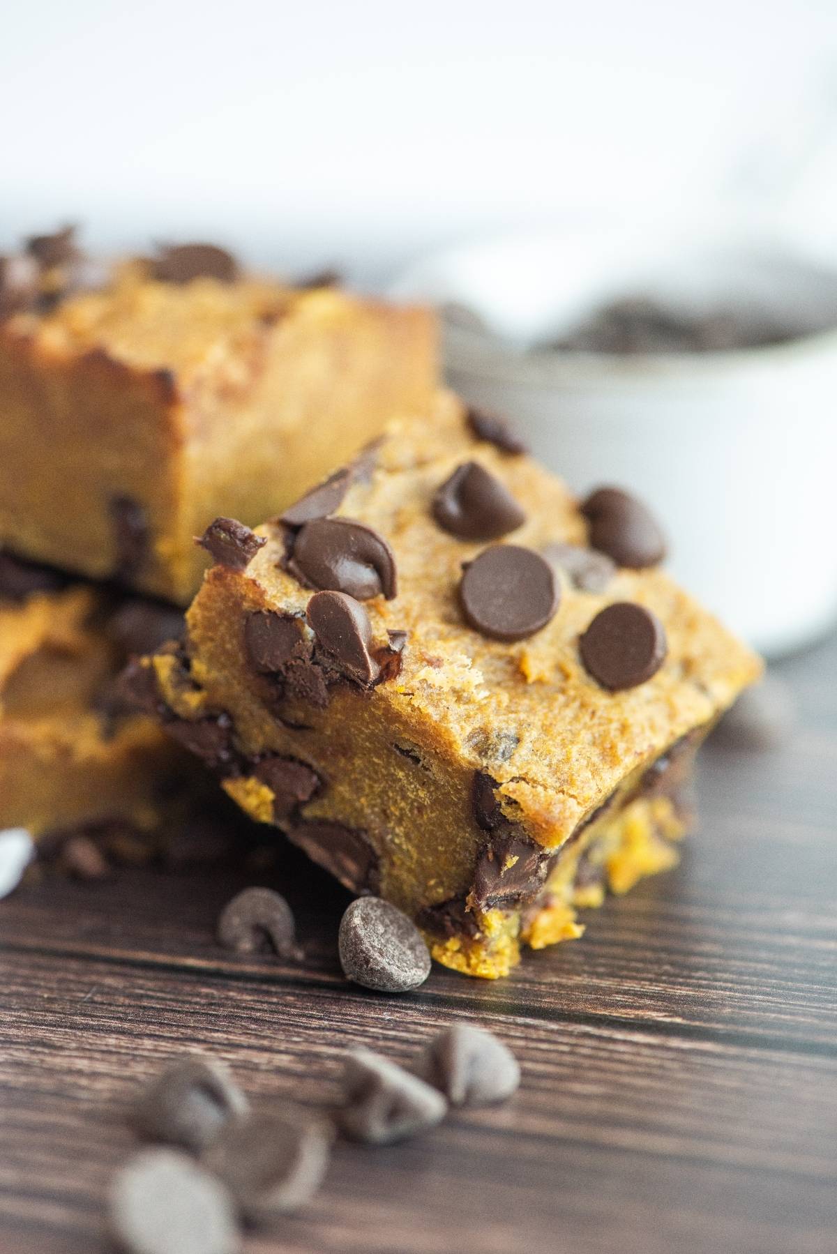 Close-up of pumpkin squares with chocolate chips stacked on a wooden surface, highlighting how pumpkin and chocolate go together perfectly, with chocolate chips scattered around.
