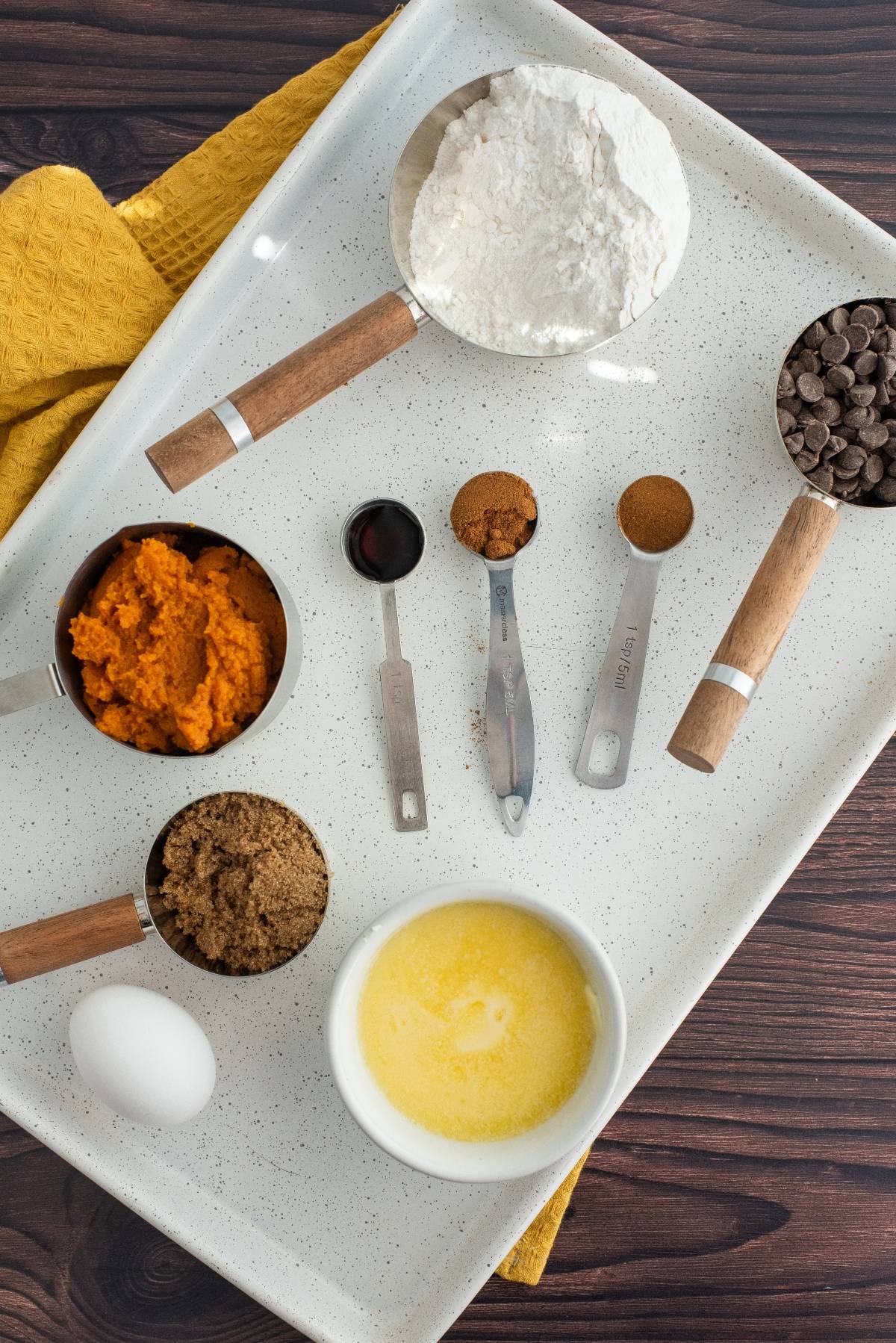 Baking ingredients on a tray: flour, pumpkin puree, chocolate chips, egg, melted butter, brown sugar, spices, vanilla—everything you need for an easy pumpkin squares recipe with chocolate chips.
