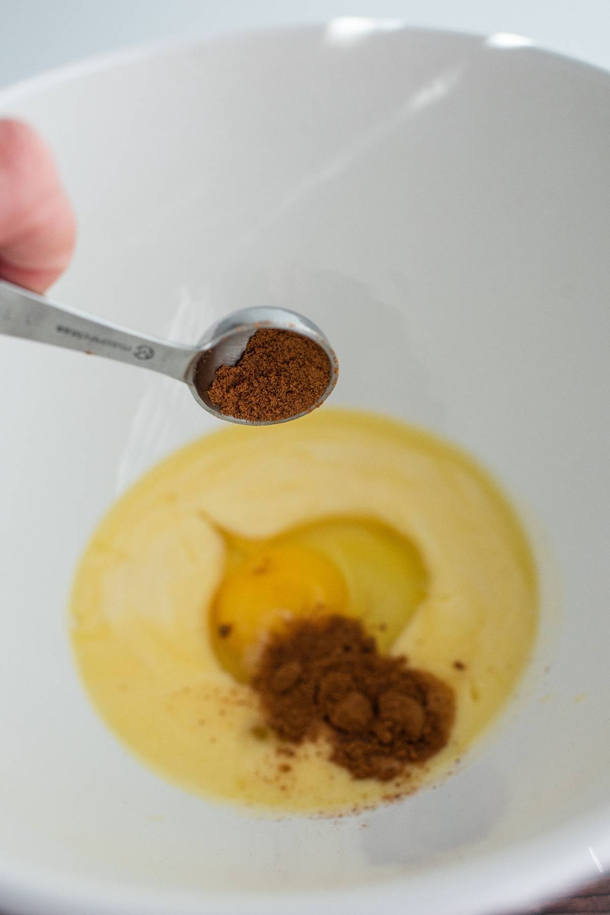 A spoon adds ground spice to a bowl with egg and creamy ingredients, the first step in our easy pumpkin squares recipe—because pumpkin and chocolate go together perfectly in these delicious pumpkin chocolate chip bars.