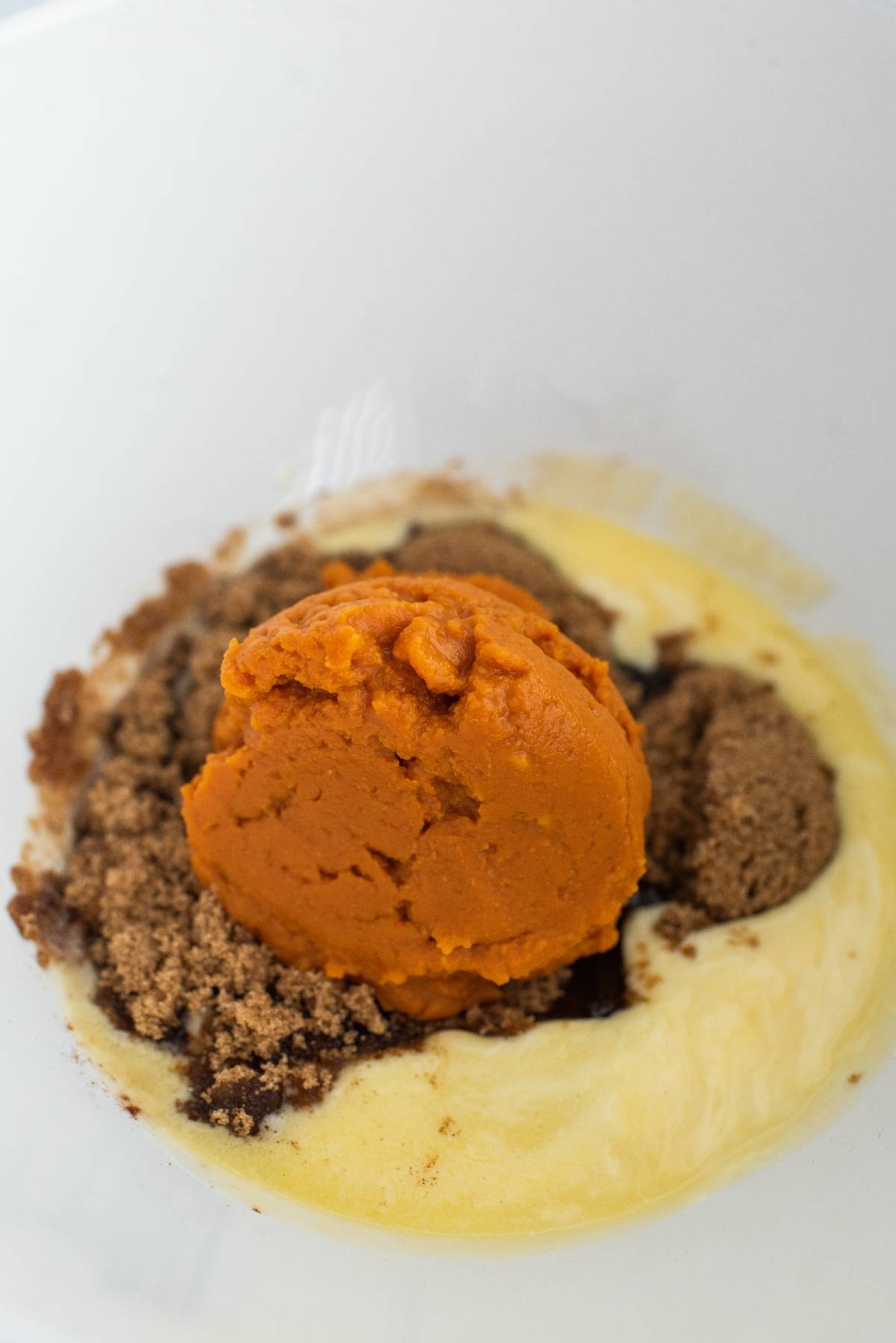 Pumpkin puree, brown sugar, and beaten egg mixture in a white mixing bowl—the perfect base for delicious pumpkin squares with chocolate chips.
