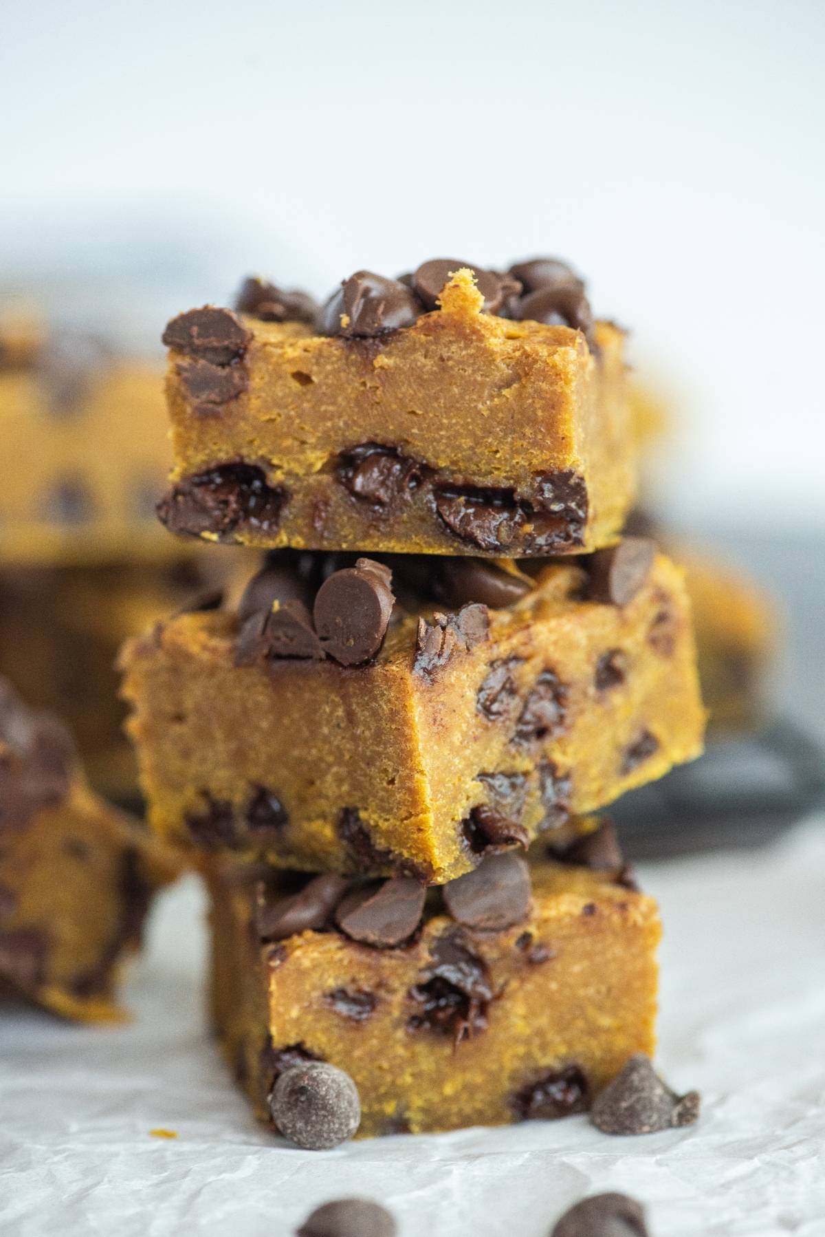 Three pumpkin chocolate chip bars stacked on each other, topped and filled with chocolate chips—proof that pumpkin and chocolate go together perfectly.