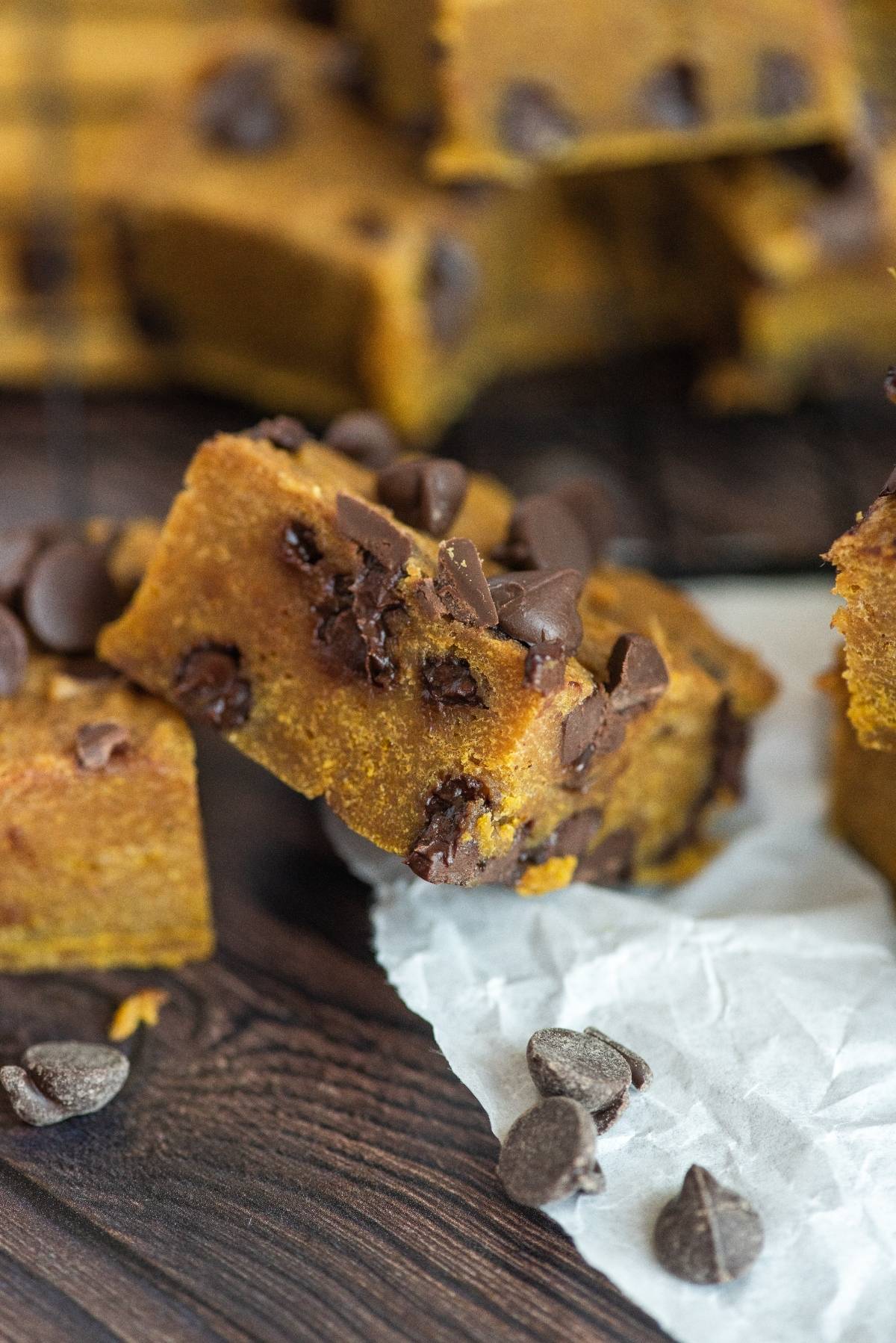 Chocolate chip pumpkin bars on parchment paper, with chocolate chips scattered on a wooden surface—proof that pumpkin and chocolate go together perfectly in this irresistible pumpkin and chocolate recipe.
