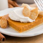 A slice of pumpkin slab pie bar topped with whipped cream and pastry leaves on a white plate with cinnamon sticks.