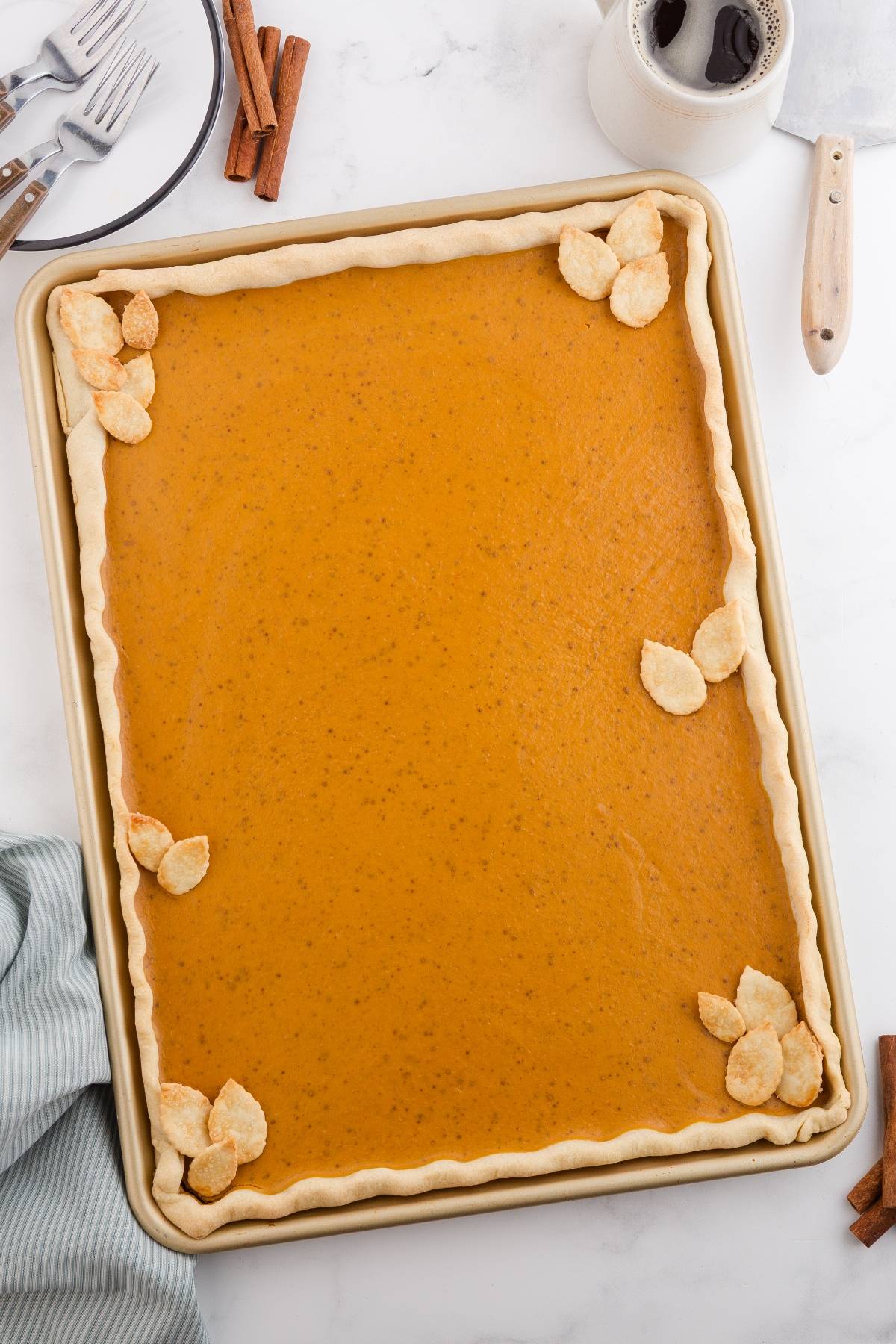 Rectangular pumpkin slab pie with a crimped crust and leaf-shaped decorations, on a baking sheet.