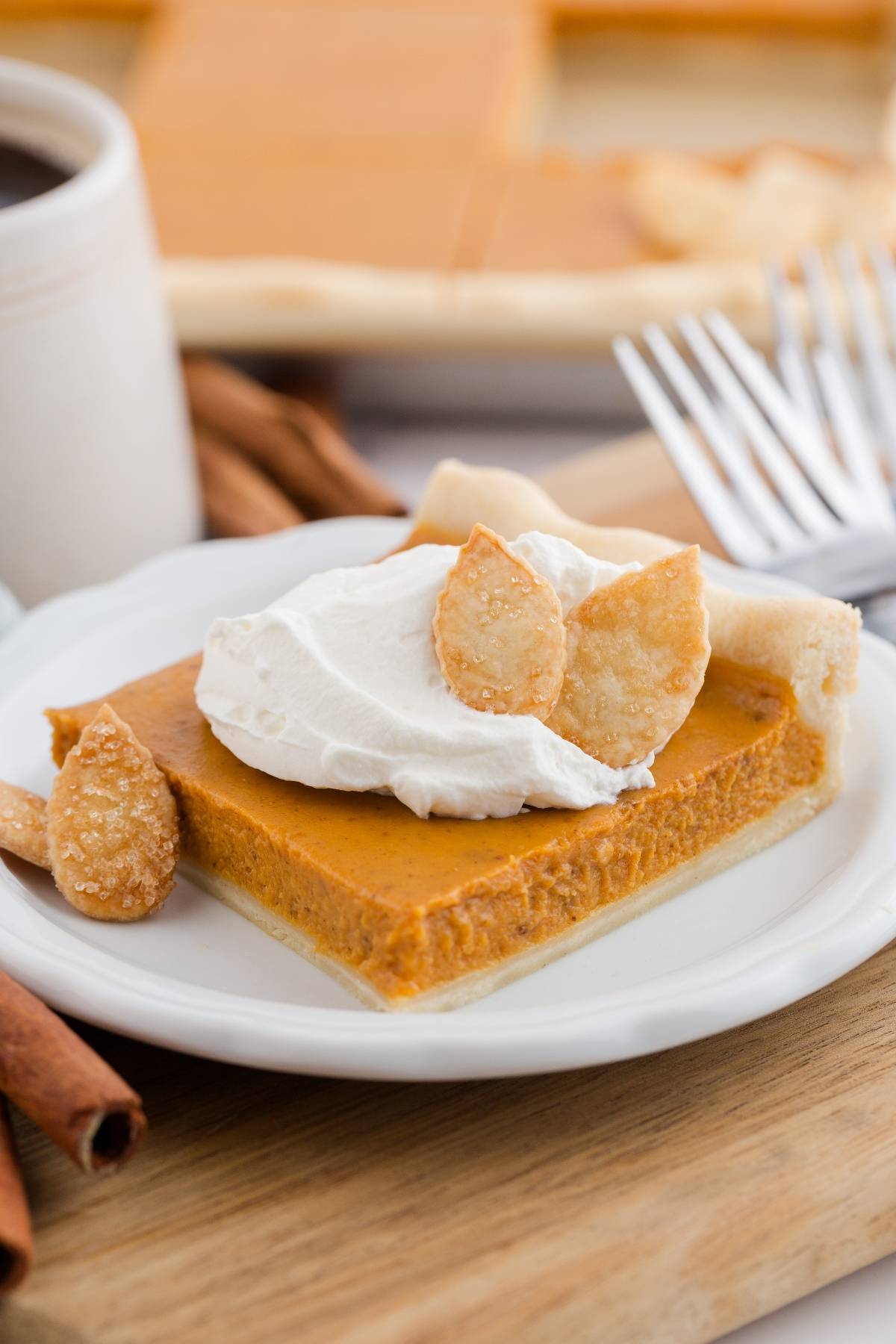A slice of pumpkin pie topped with whipped cream and pastry leaves on a white plate.