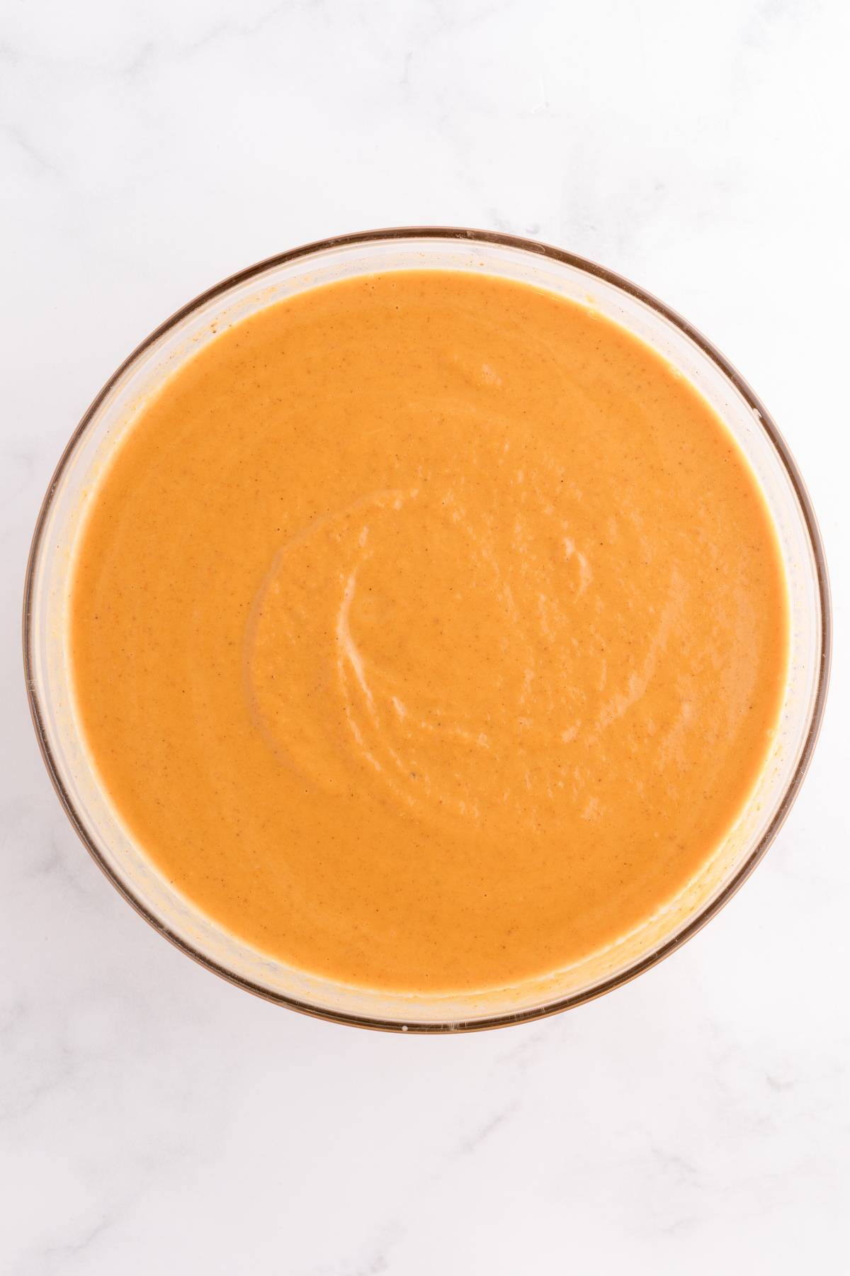 A glass bowl filled with creamy orange soup on a white marble surface.