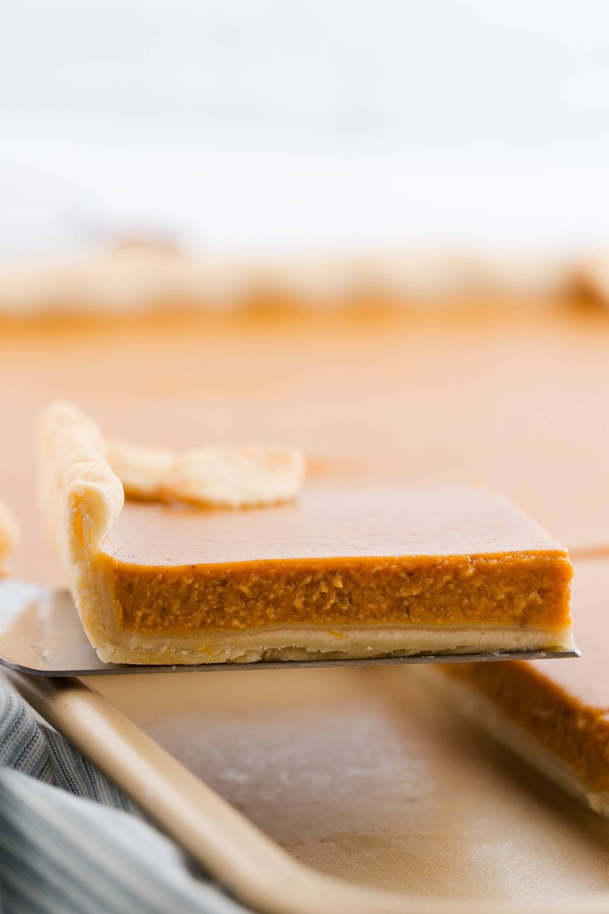 A close-up of a slice of pumpkin pie bar with a flaky crust being lifted from a baking tray.