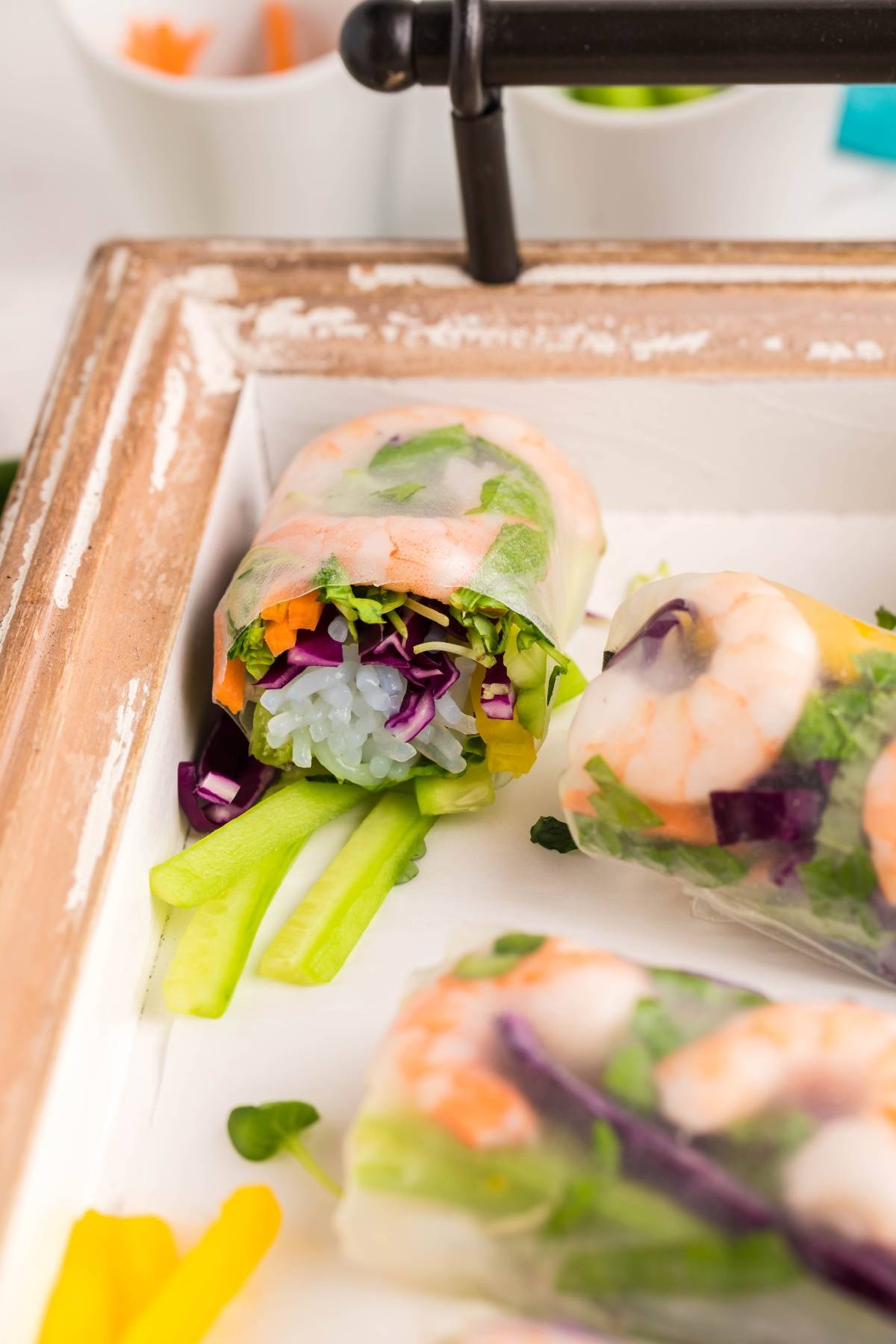 Fresh shrimp spring rolls filled with rice noodles, carrots, cabbage, and greens on a tray with celery sticks—perfect to pair with your favorite dipping sauce for spring rolls.