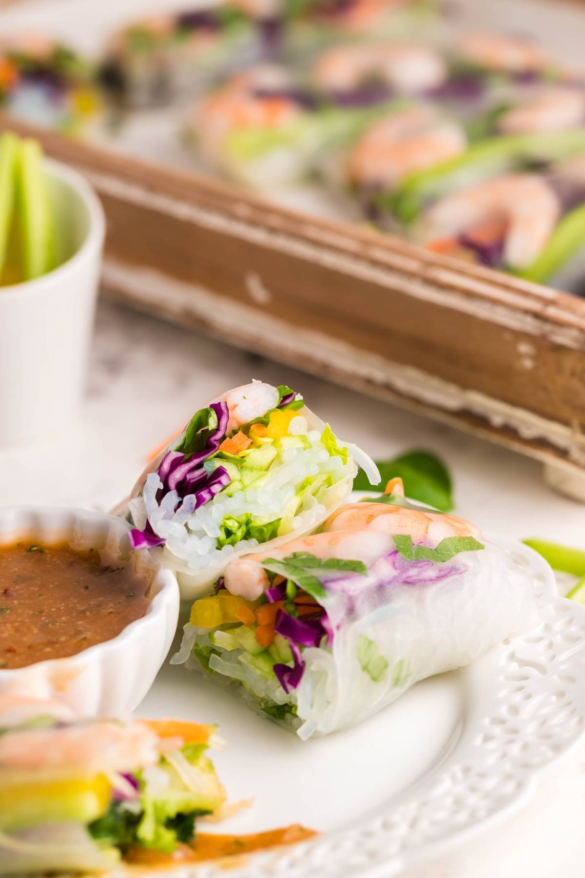 Two fresh shrimp spring rolls filled with crisp vegetables and shrimp, one sliced open to reveal the filling, are served alongside a spicy garlic sauce—the perfect dipping sauce for spring rolls.