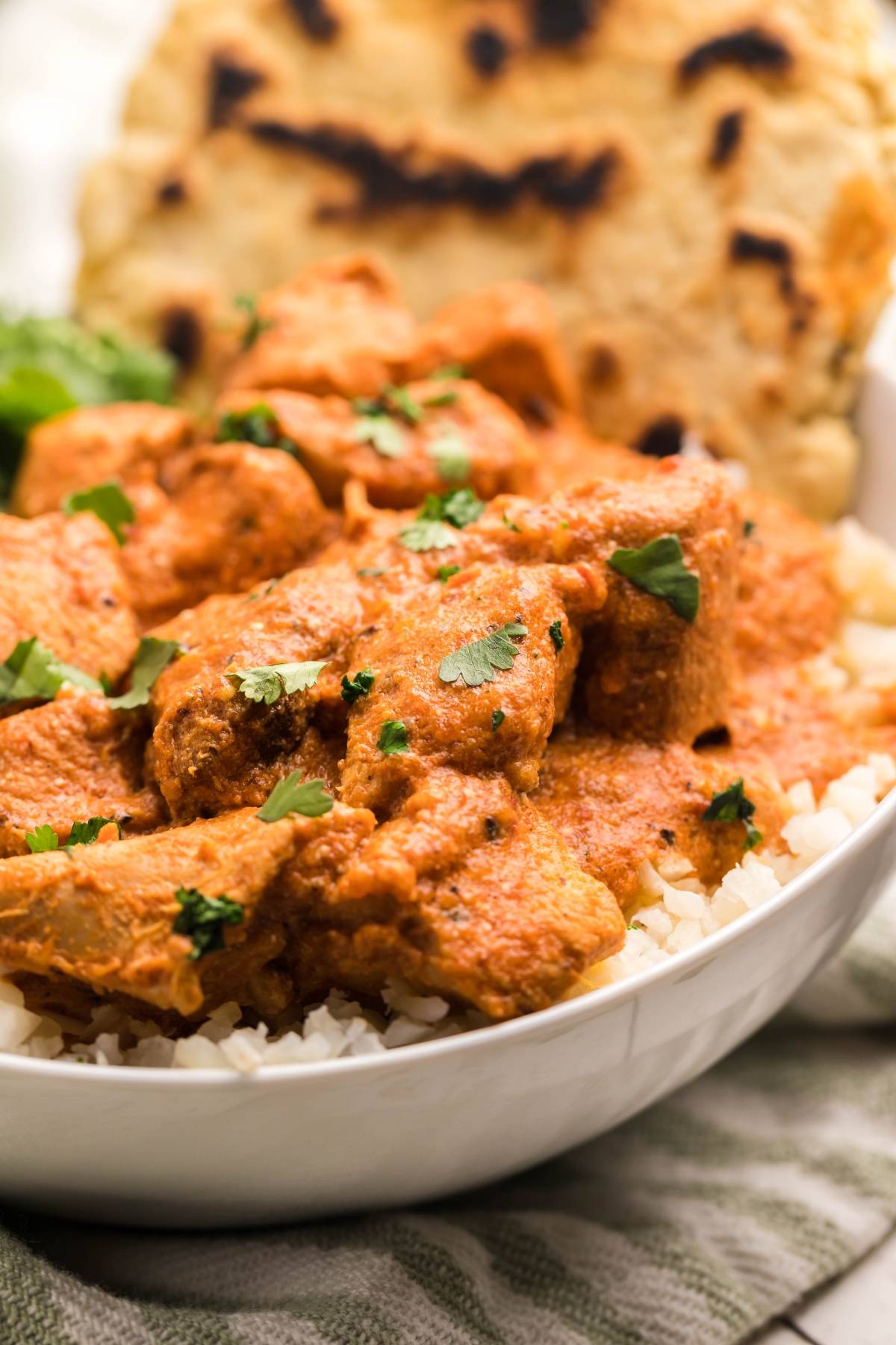 Enjoy chicken tikka masala served over rice, garnished with cilantro, with naan bread in the background—an easy slow cooker recipe perfect for weeknights.