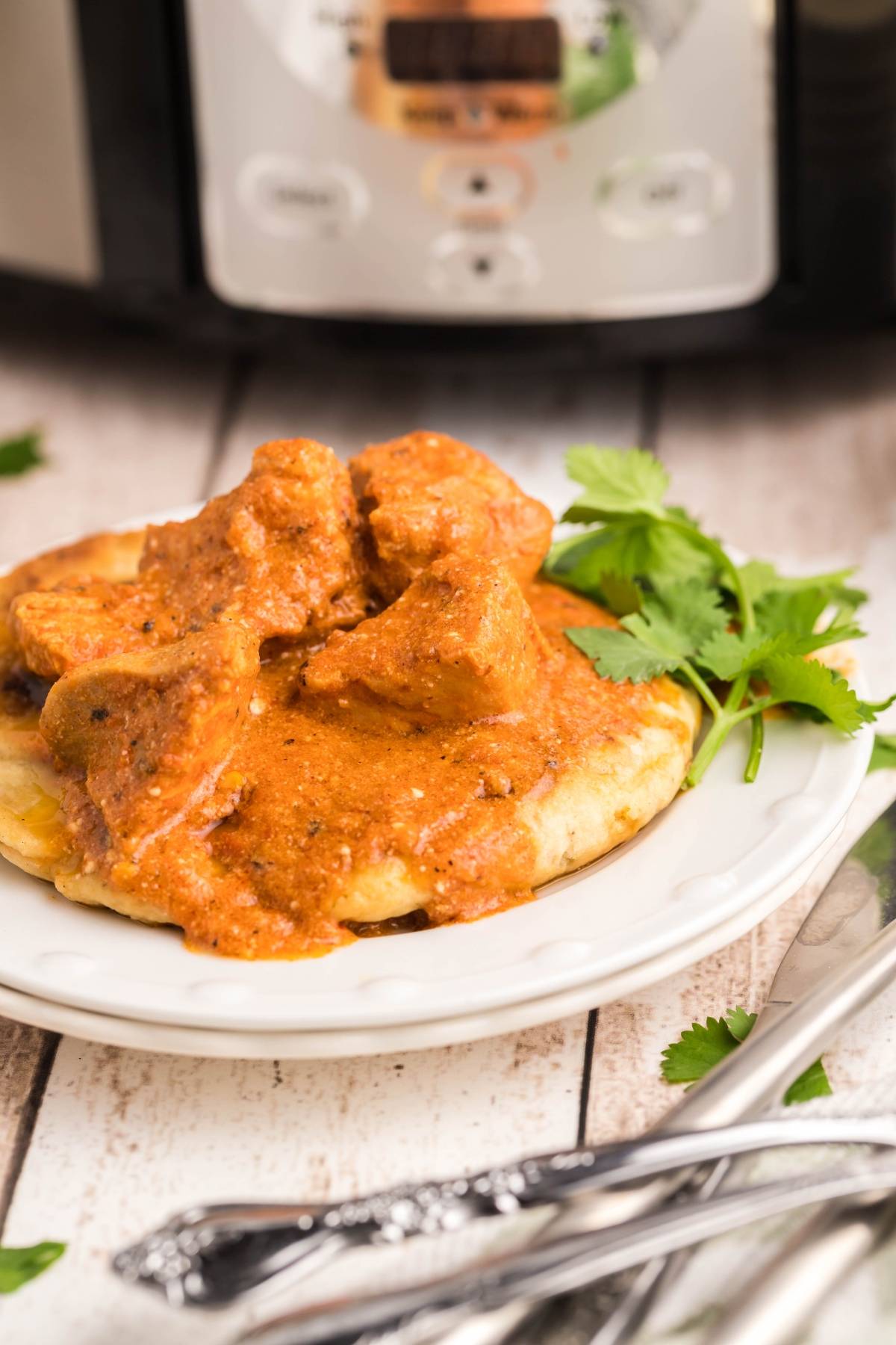 Plate of naan topped with creamy orange curry and garnished with cilantro, featuring a Chicken curry recipe made in the Instant Pot.